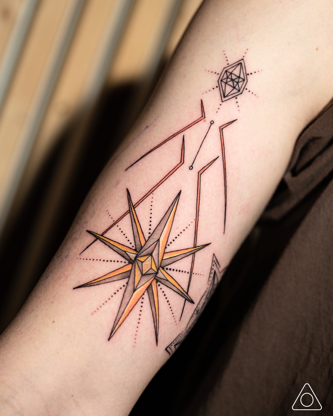 Fine-line Earth element tattoo with a compass star beacon on the front bicep, sacred geometry elemental tattoo art representing direction and grounding by 1MM Tattoo, Los Angeles, California.