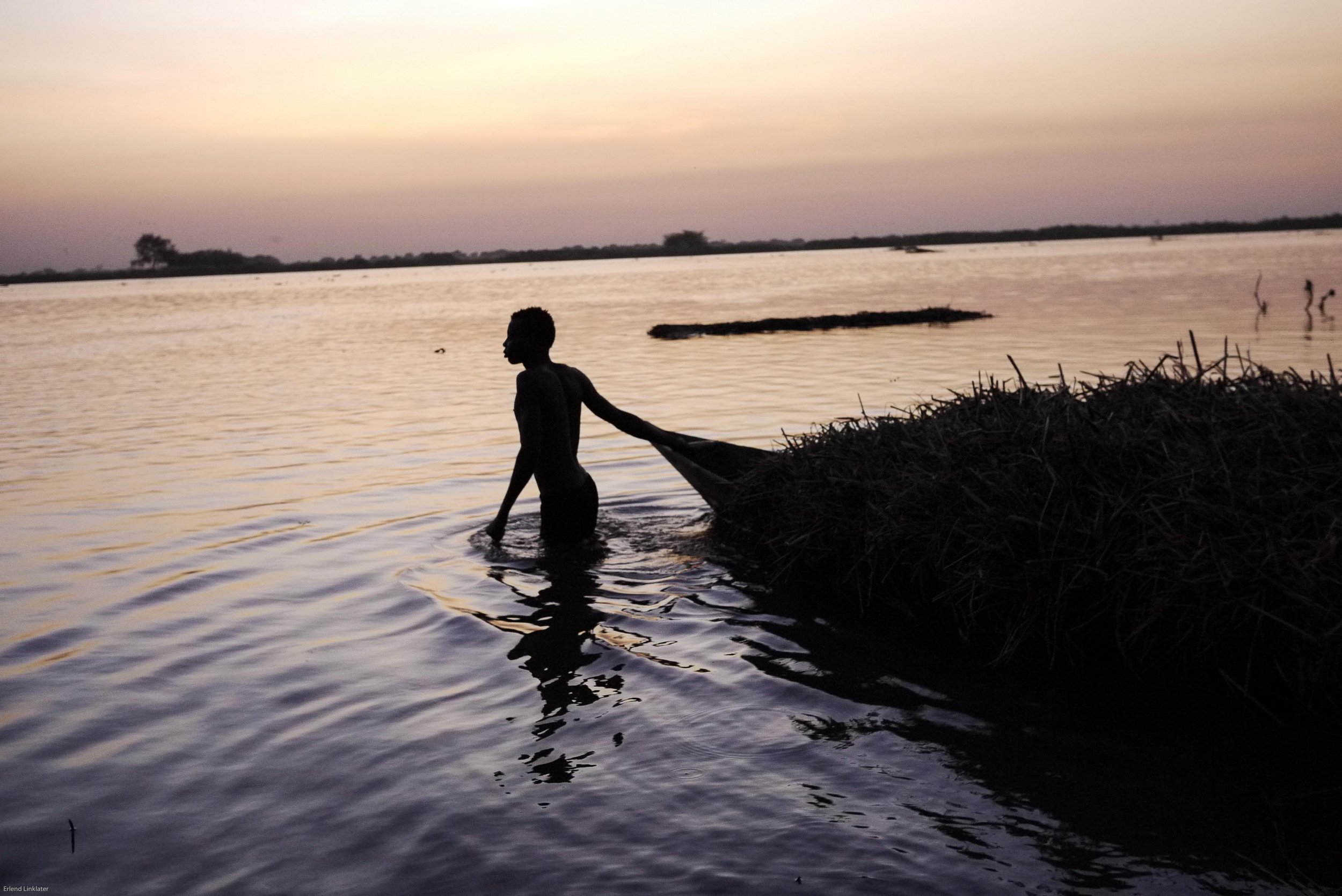 A man pulls his wooden pirogue laden with reeds to be used in house construction through the waters of the Nile, Malakal 2011. Malakal sits on the southern edge of the Sudd, a vast swamp in South Sudan whose name derives from the Arabic sadd meaning