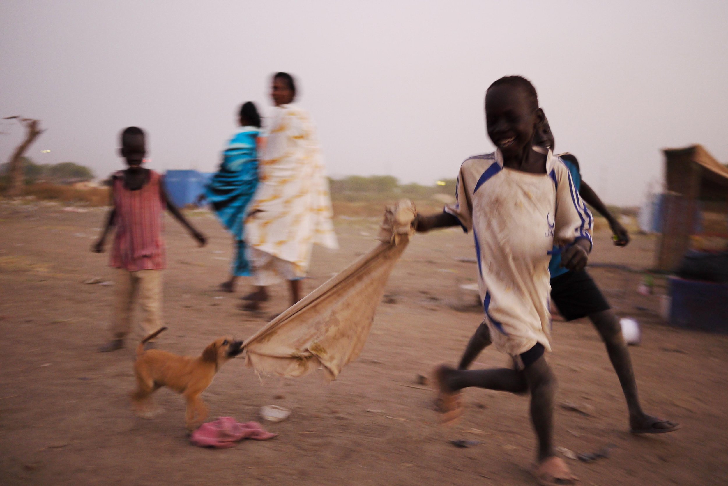 Recently returned refugees play with a puppy in a transitional camp while they await transportation to the villages where they will build new lives. After more than 30 years of conflict, the Comprehensive Peace Agreement and independence referendum