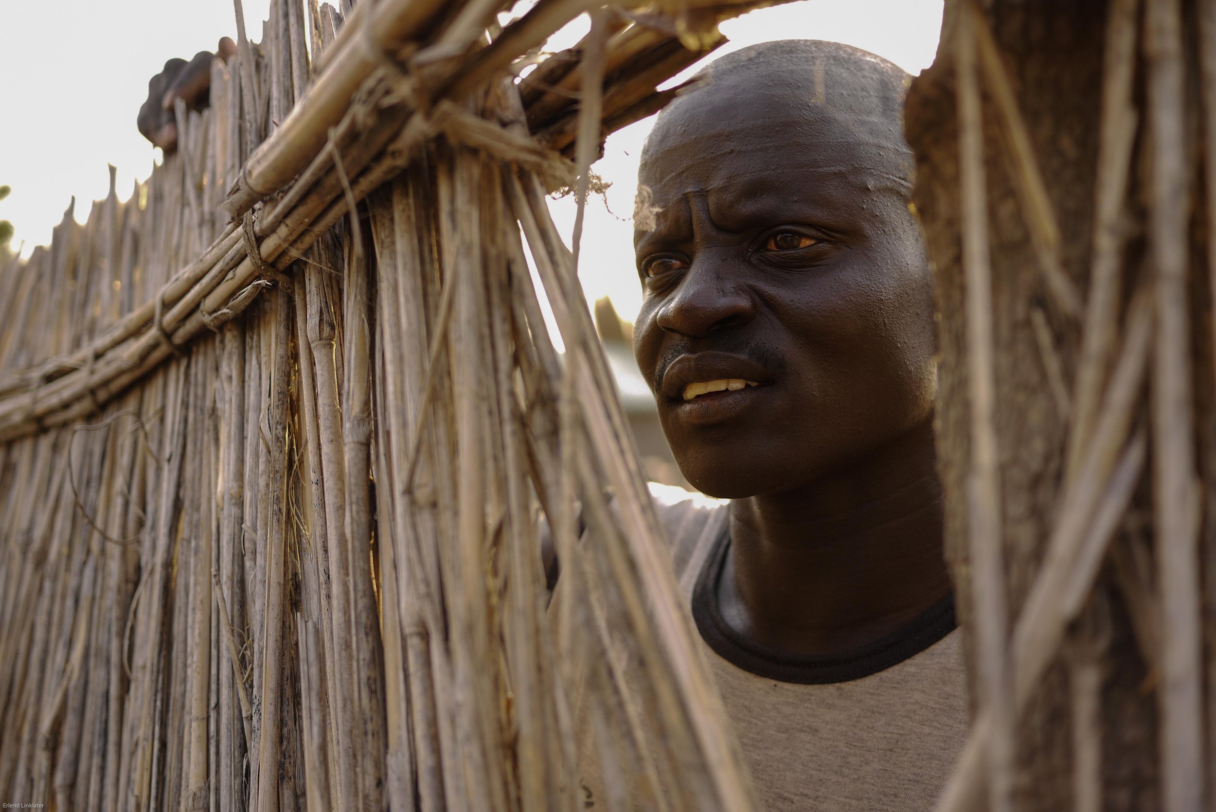A man with traditional Nuer initiation marks peers through a fence in Malakal, South Sudan. The Nuer receive facial markings (called gaar) as part of their initiation into adulthood. The pattern of Nuer scarification varies within specific subgroups