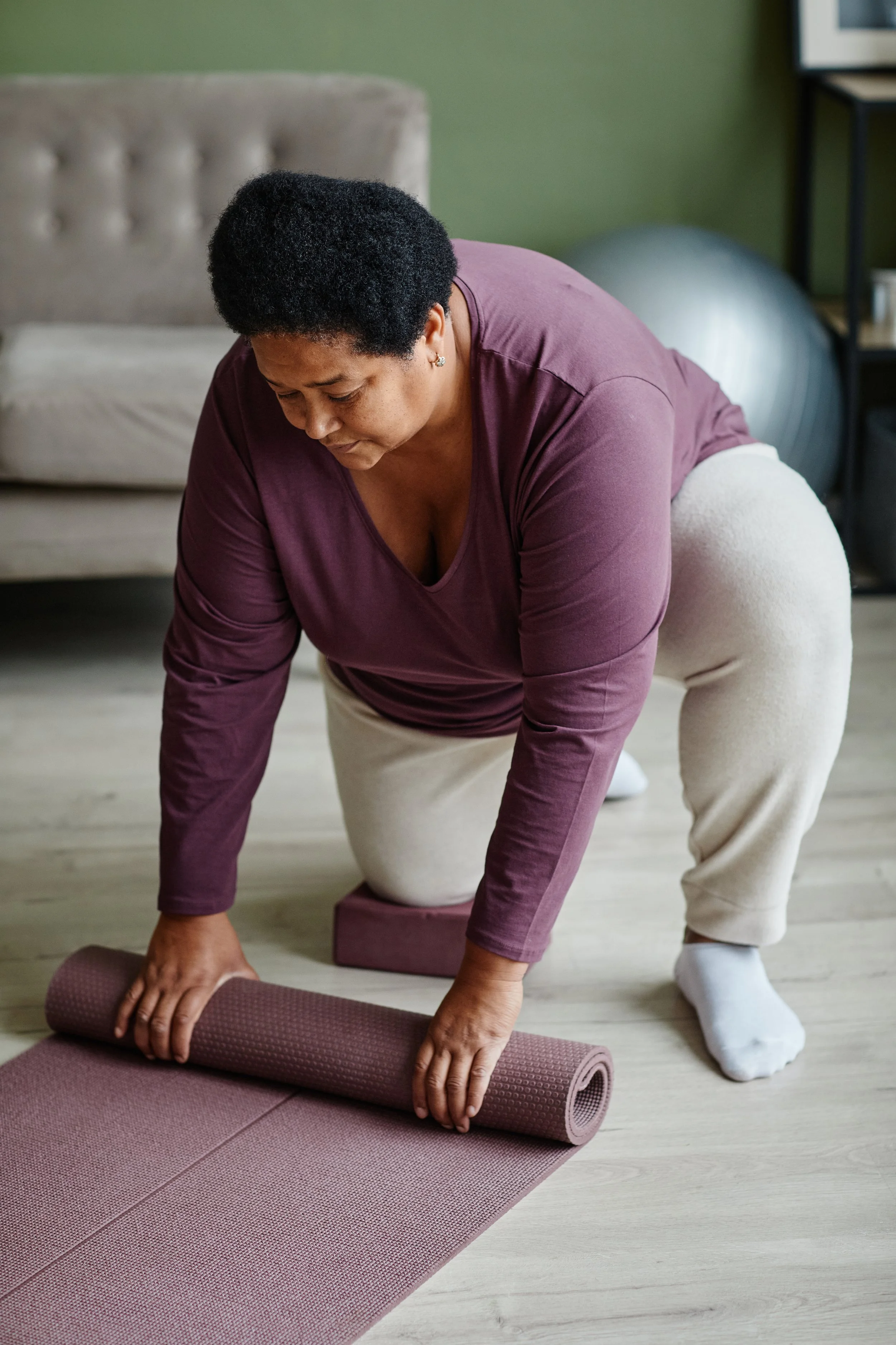 woman rolling out yoga mat, with her knee on a yoga block, accessible fitness chronic pain movement