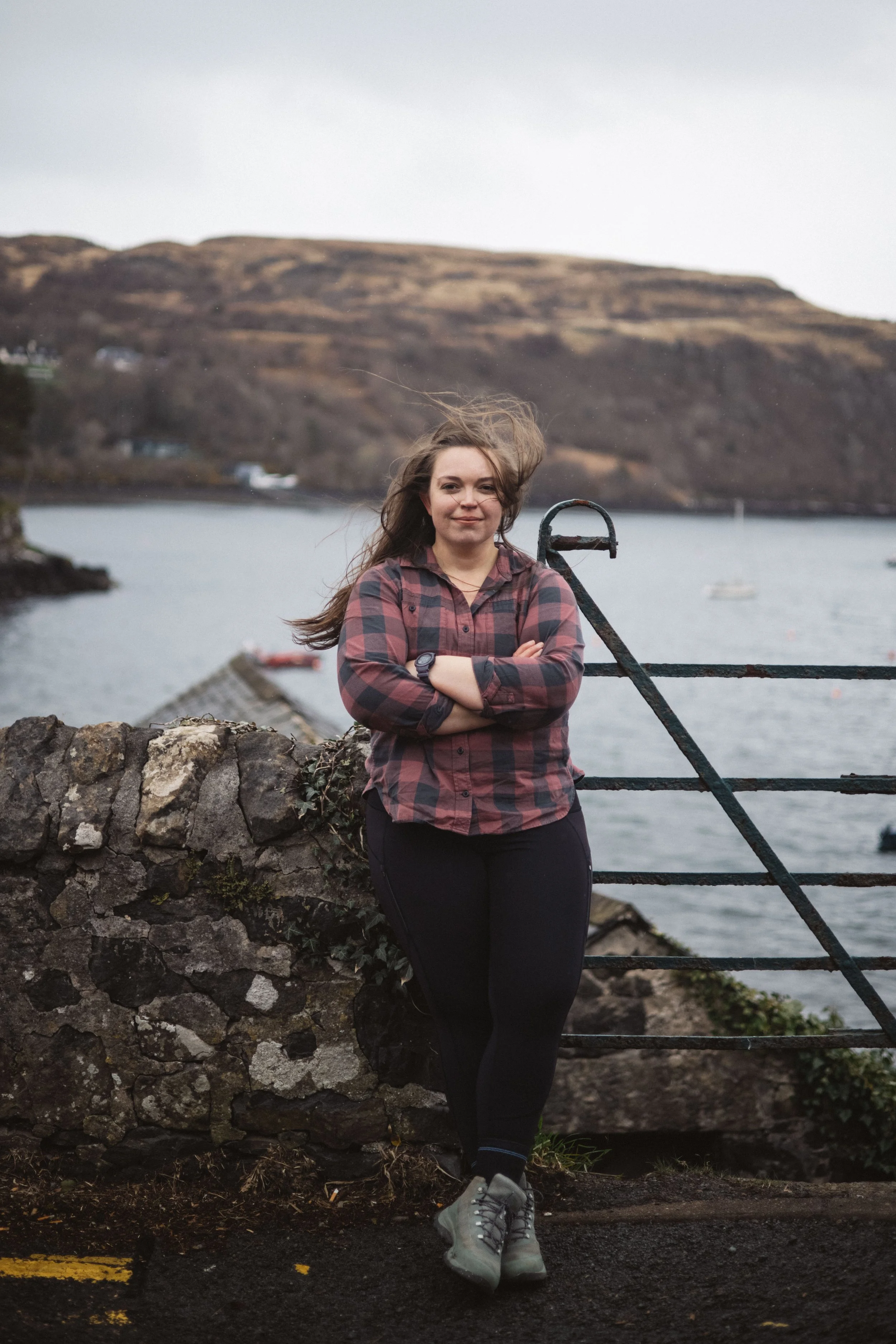 Sarah Petty leaning onto an old rock wall overlooking an island bay. Movement for reconnecting with your body