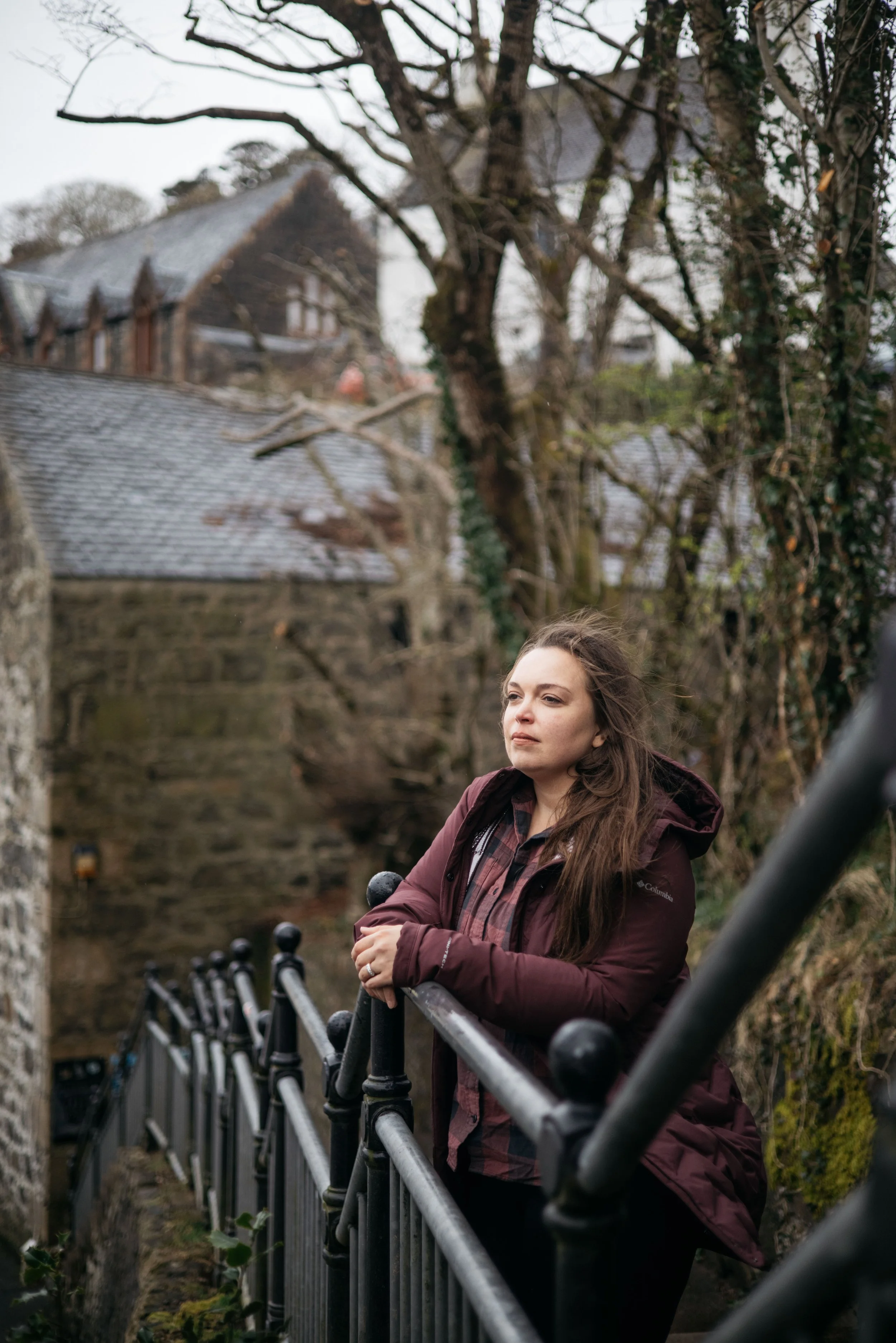 Sarah Petty standing with hands on a railing, looking out with old buildings behind her