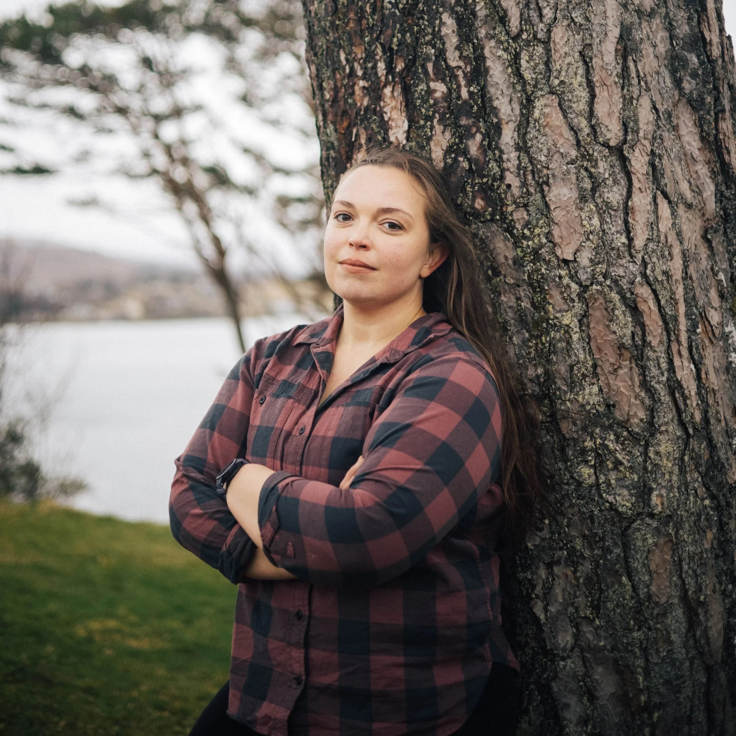 Coach Sarah is a mid-size white woman with long dark hair. She is standing against a tree with her arms crossed