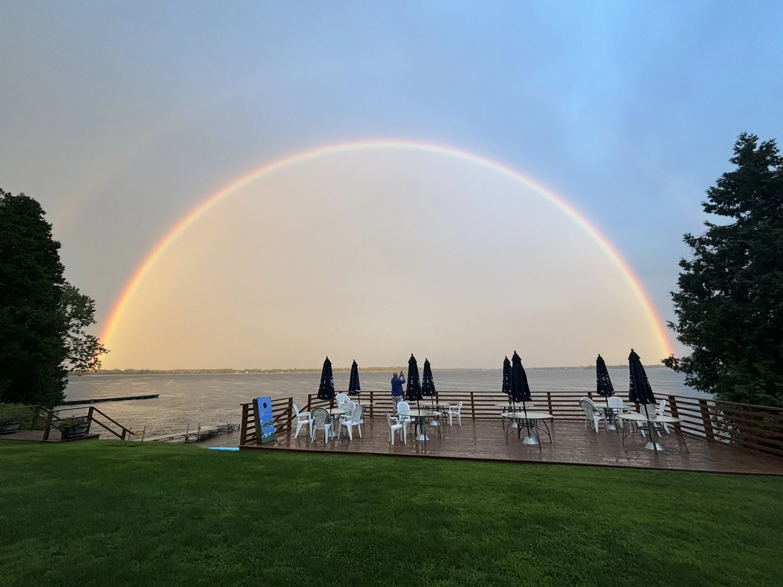 a wooden porch with picnic tables overlooking the lake, with a full rainbow framing the view