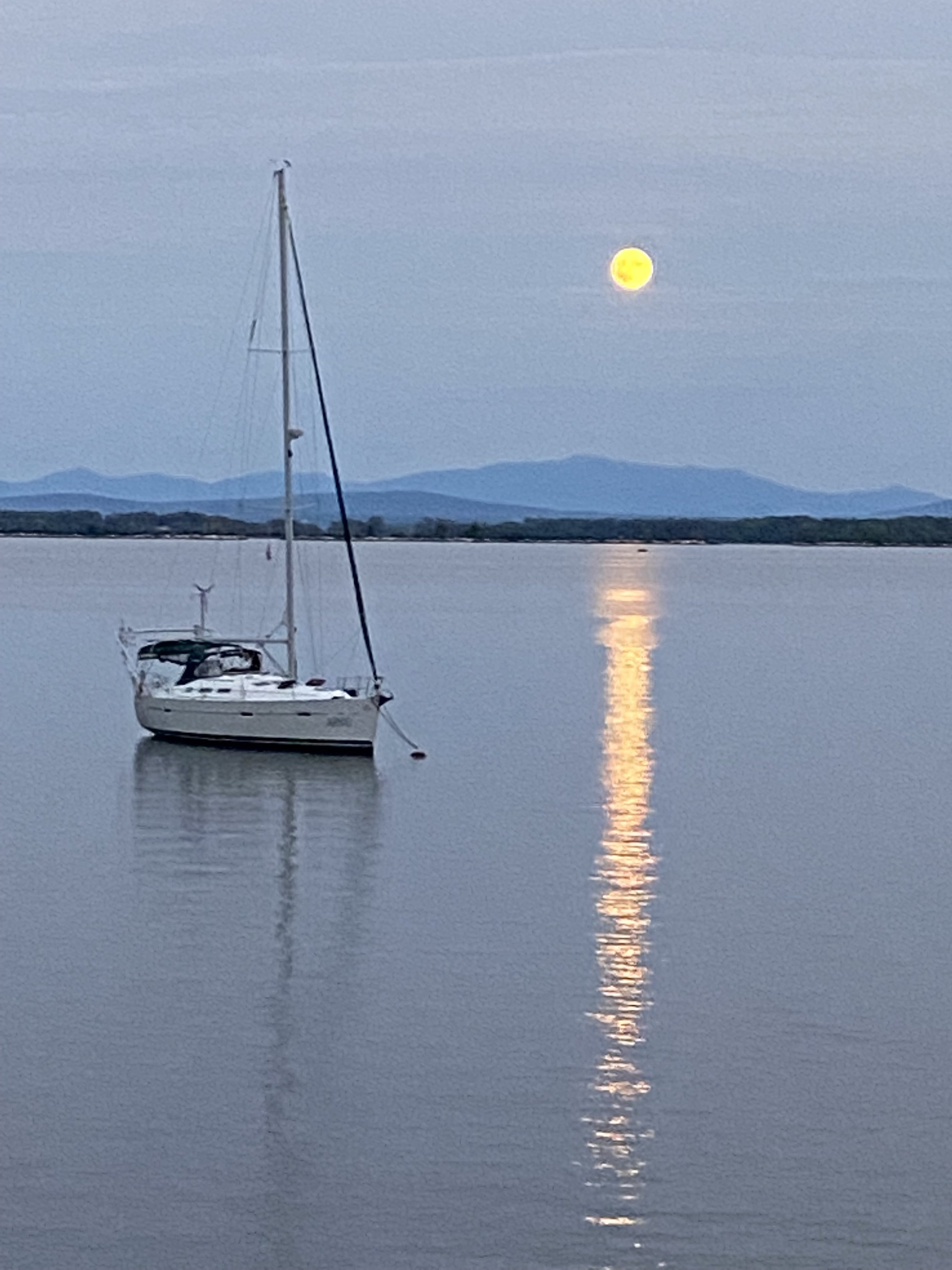 a sailboat moored on the lake, with a view of the Green Mountains and the moon in the background