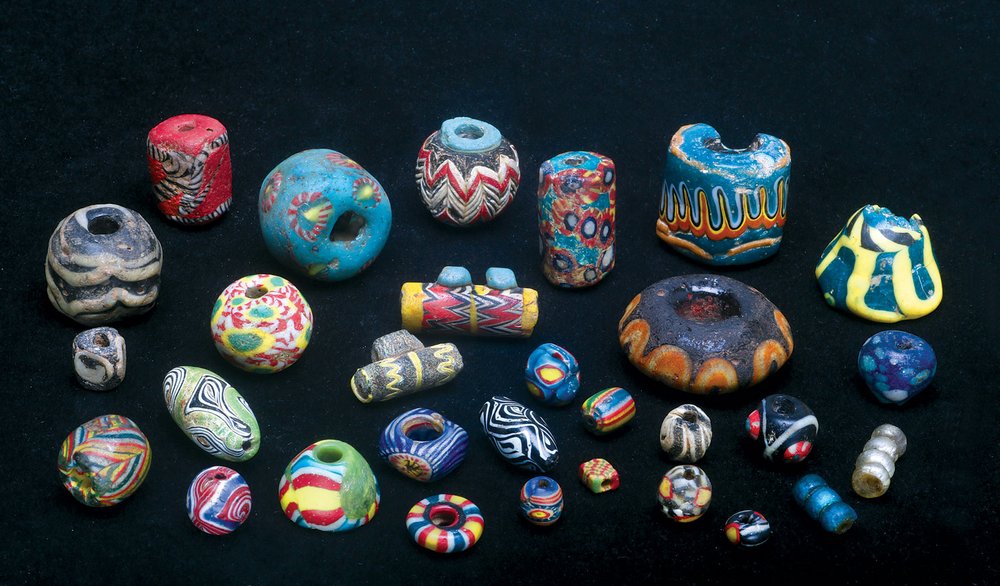  ISLAMIC GLASS BEADS FROM SYRIA, MAURITANIA, CRIMEA, AND HEBRON, including one large broken turquoise bead with orange trailing from Turkey, originally made in Hebron, Palestine, as well as large bicone black bead with orange/yellow trailing. Adjacen