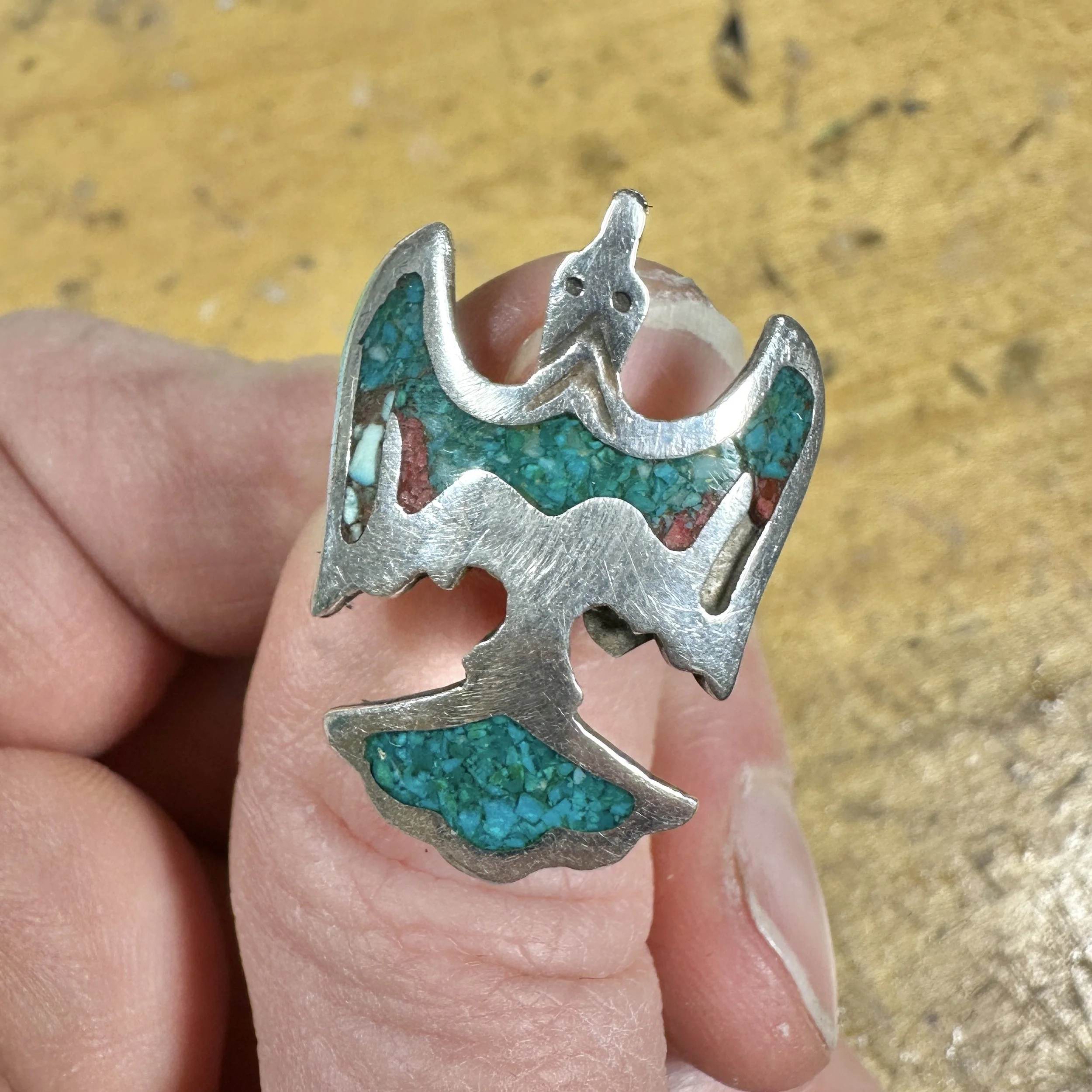 Because of now thin the silver is in the wings, it ended up cracking the inlay when bent. The left side has already been poorly repaired with a lighter colored turquoise, and the right side is missing the red coral.
