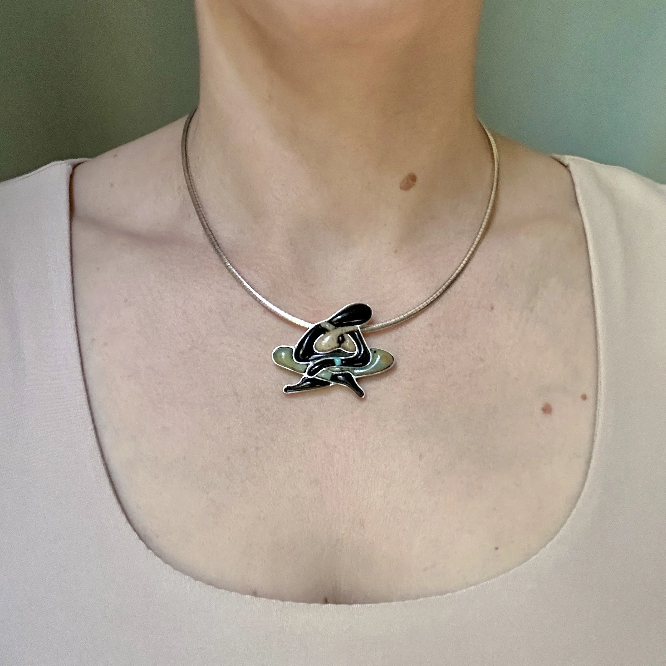 Figurative cobblestone inlay pendant of sitting female set in sterling silver; picture of pendant modeled on the lapidary jewelry artist Caitlin Albritton