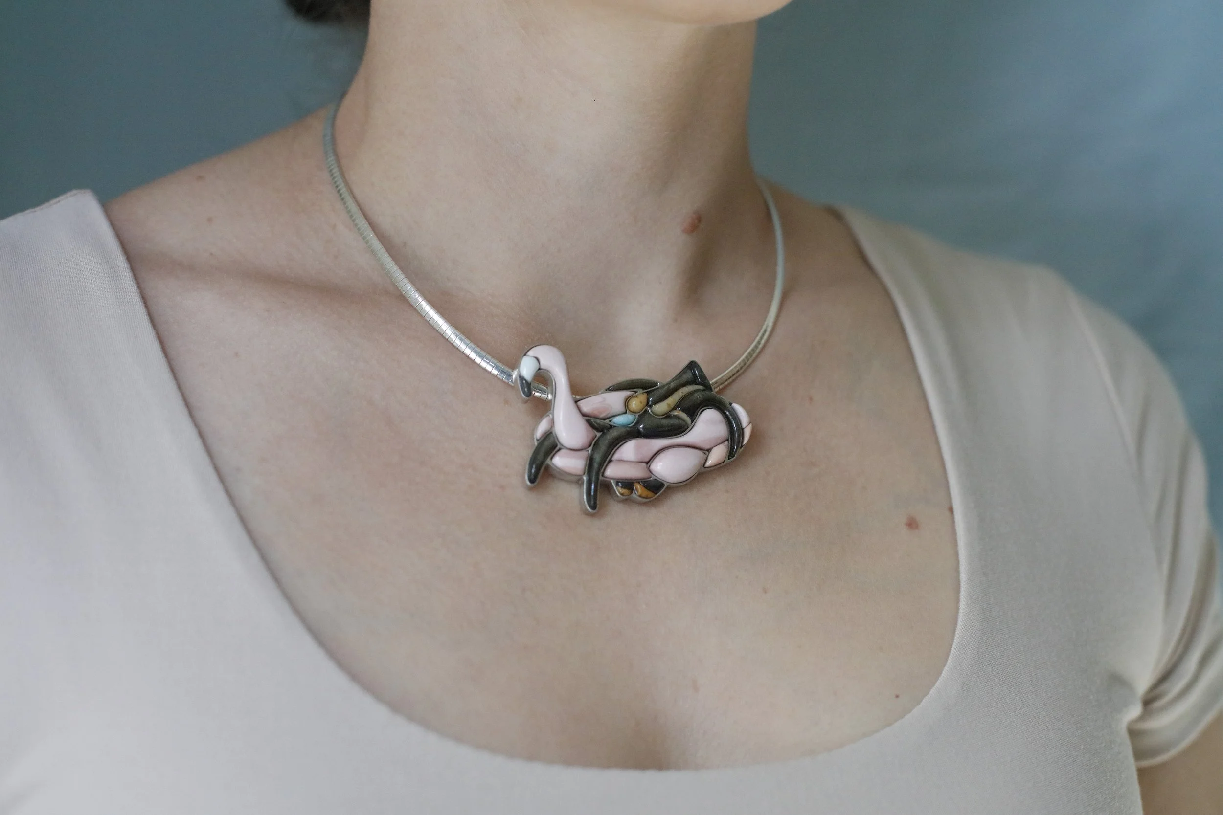 Side view, cobblestone inlay pendant of a woman riding a flamingo float with hand-cut Australian pink opal, gold sheen obsidian, and other natural stones