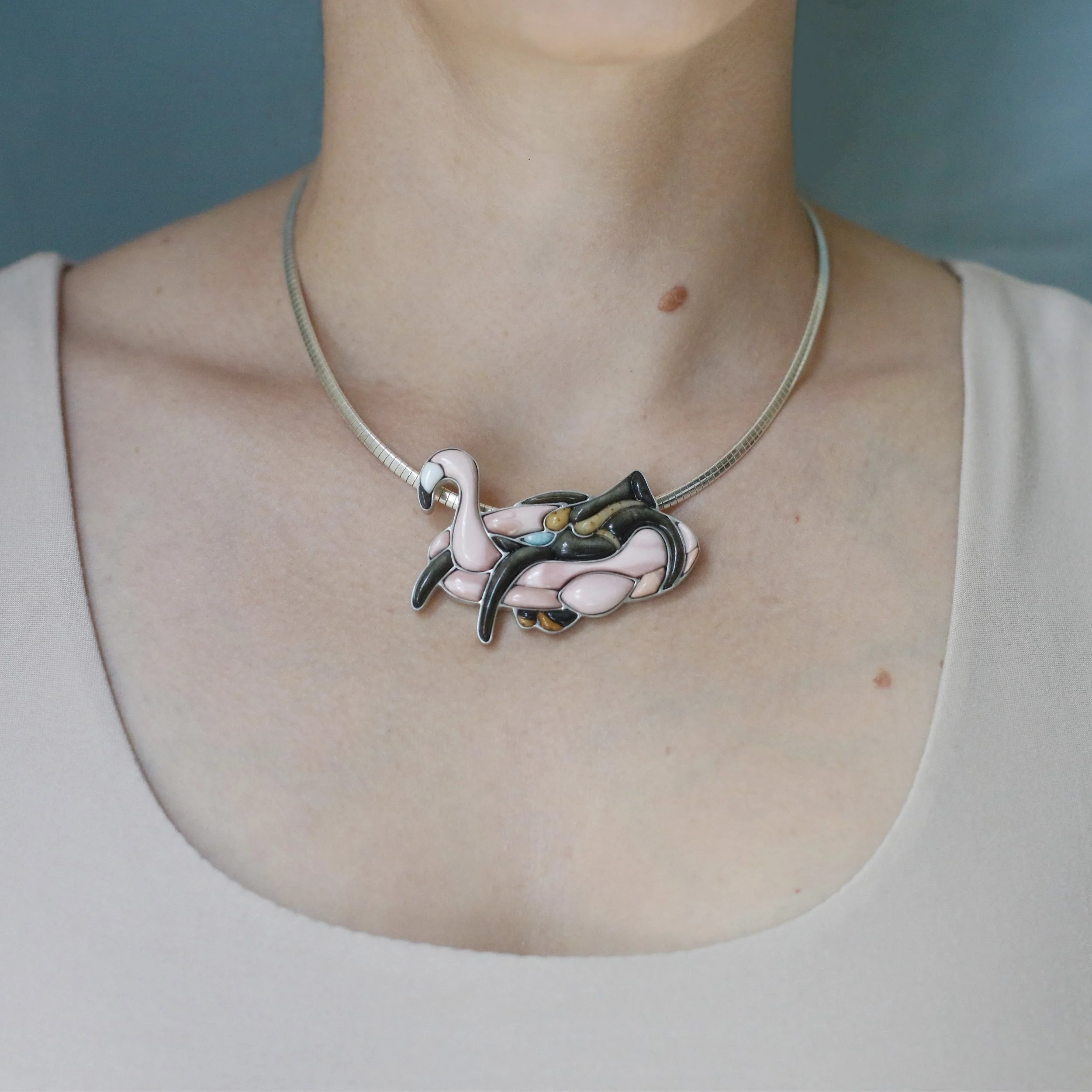 Figurative inlay pendant of a girl riding a flamingo float, modeled by the lapidary jewelry artist Caitlin Albritton
