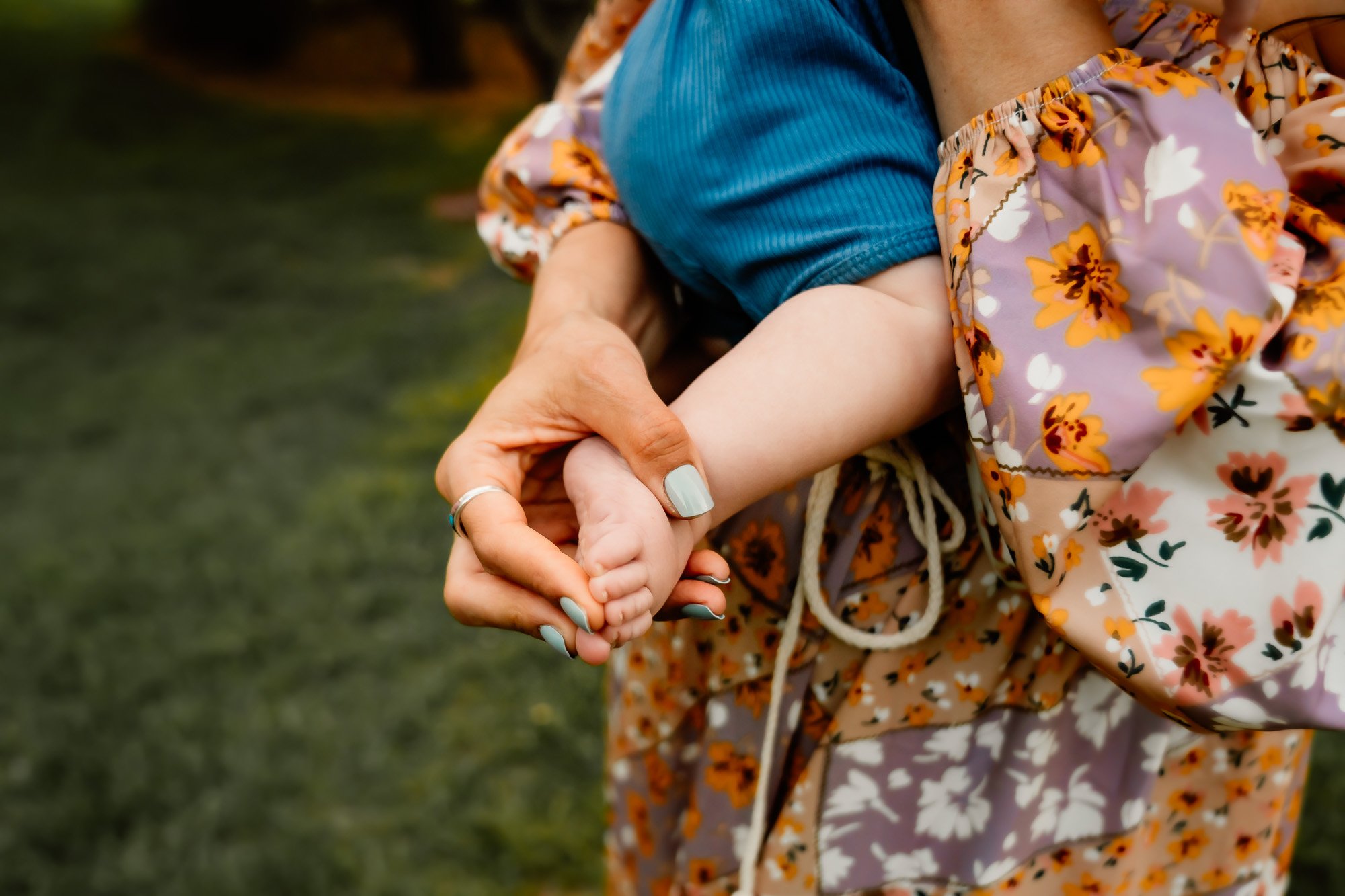 close-up of a mother holding her baby's tiny foot, with a floral dress in the background