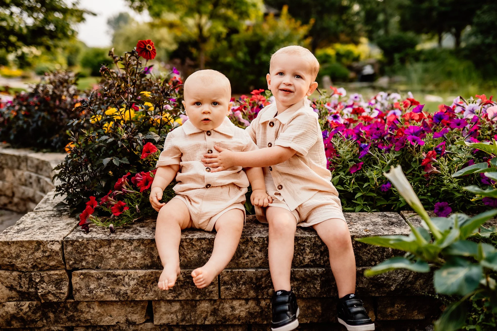 Two young brothers sitting together and smiling on a stone wall during an outdoor family session in Rochester MN
