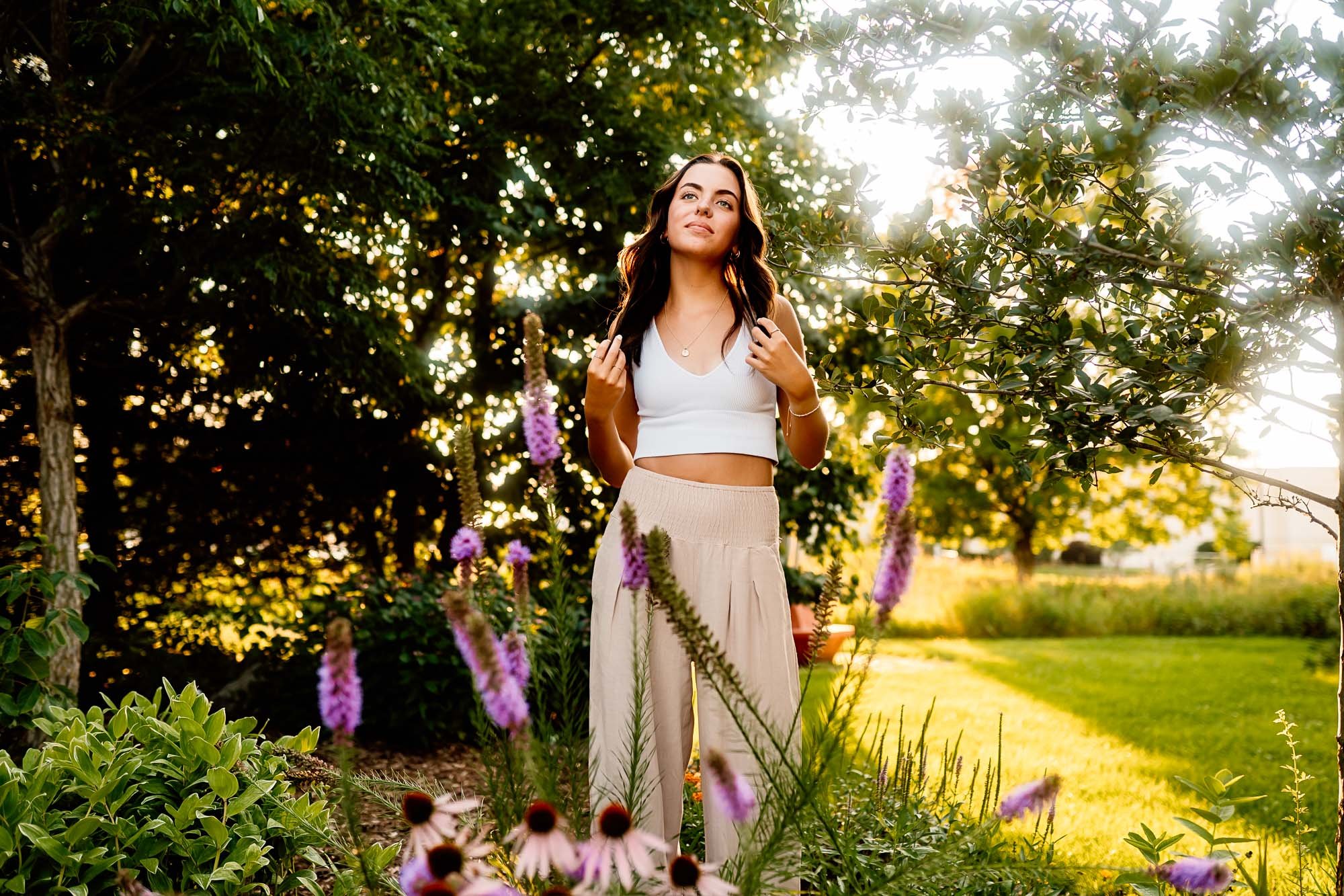 High school senior posing carefree with purple flowers and sun behind her