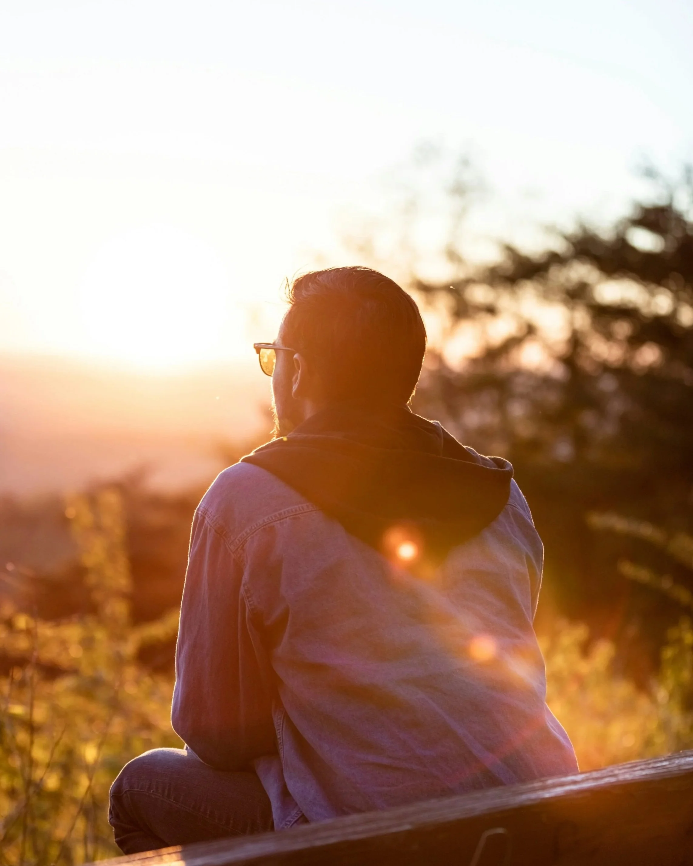 Person sitting on a bench at sunset, quietly reflecting while overlooking a natural landscape at the end of the day.