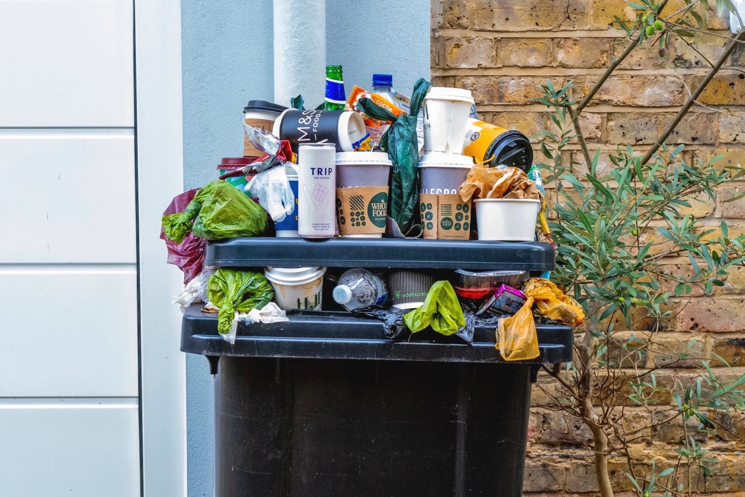 Overflowing garbage bin filled with single-use containers and plastic waste, highlighting the environmental impact of overconsumption