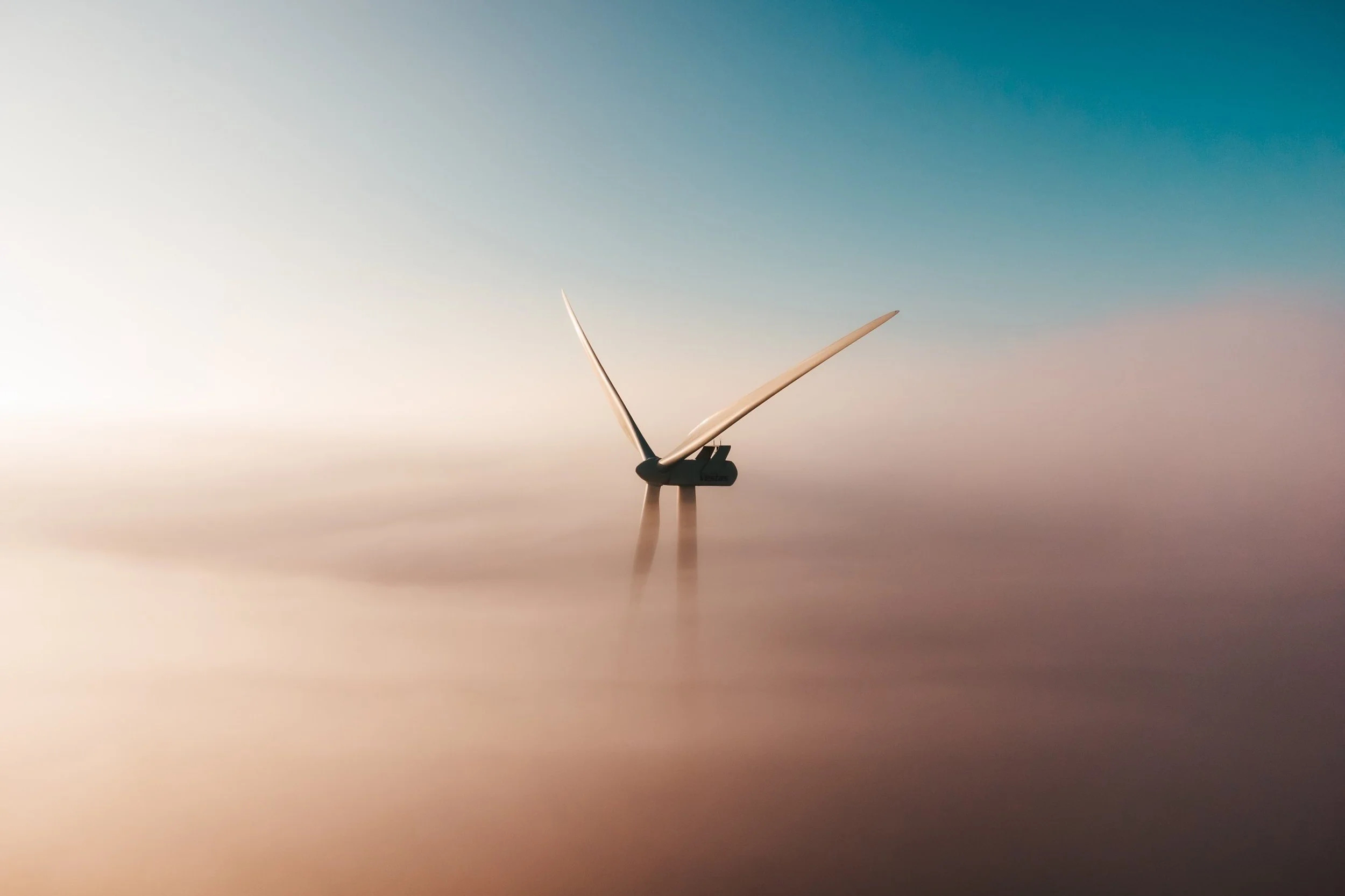 Wind turbine rising above clouds at sunrise, representing clean renewable energy and low-carbon power solutions