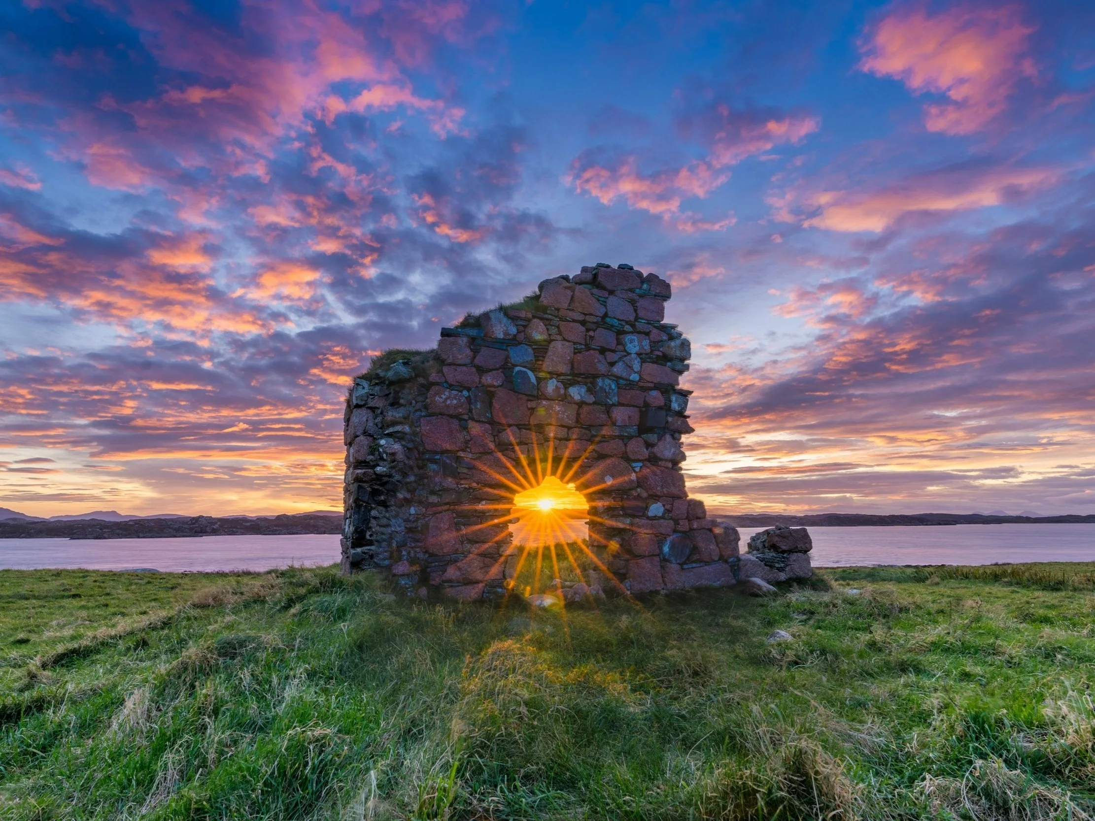 Golden sunset shining through an ancient stone ruin by the sea in Ireland, beneath a vibrant, cloud-streaked sky.