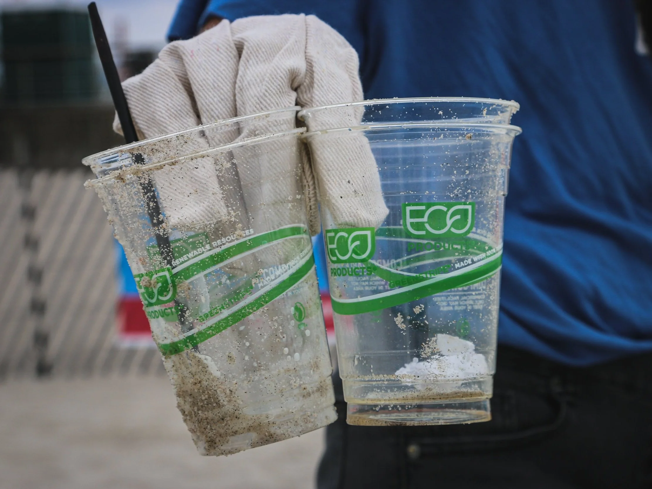 Greenwashed eco-friendly plastic cups with green labels held on a sandy beach