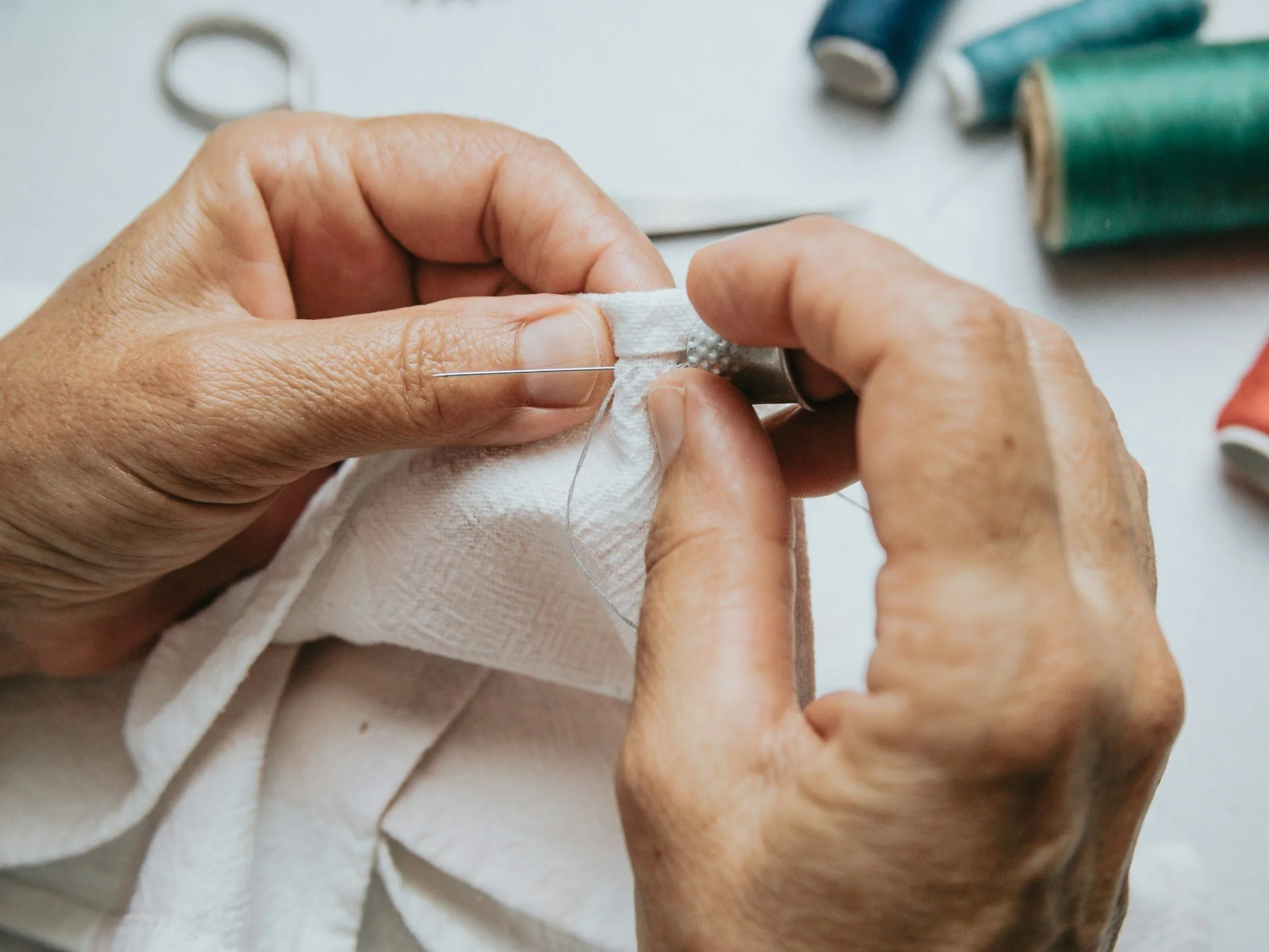 Hands sewing fabric with needle and thread to extend garment life and promote sustainable, circular fashion.