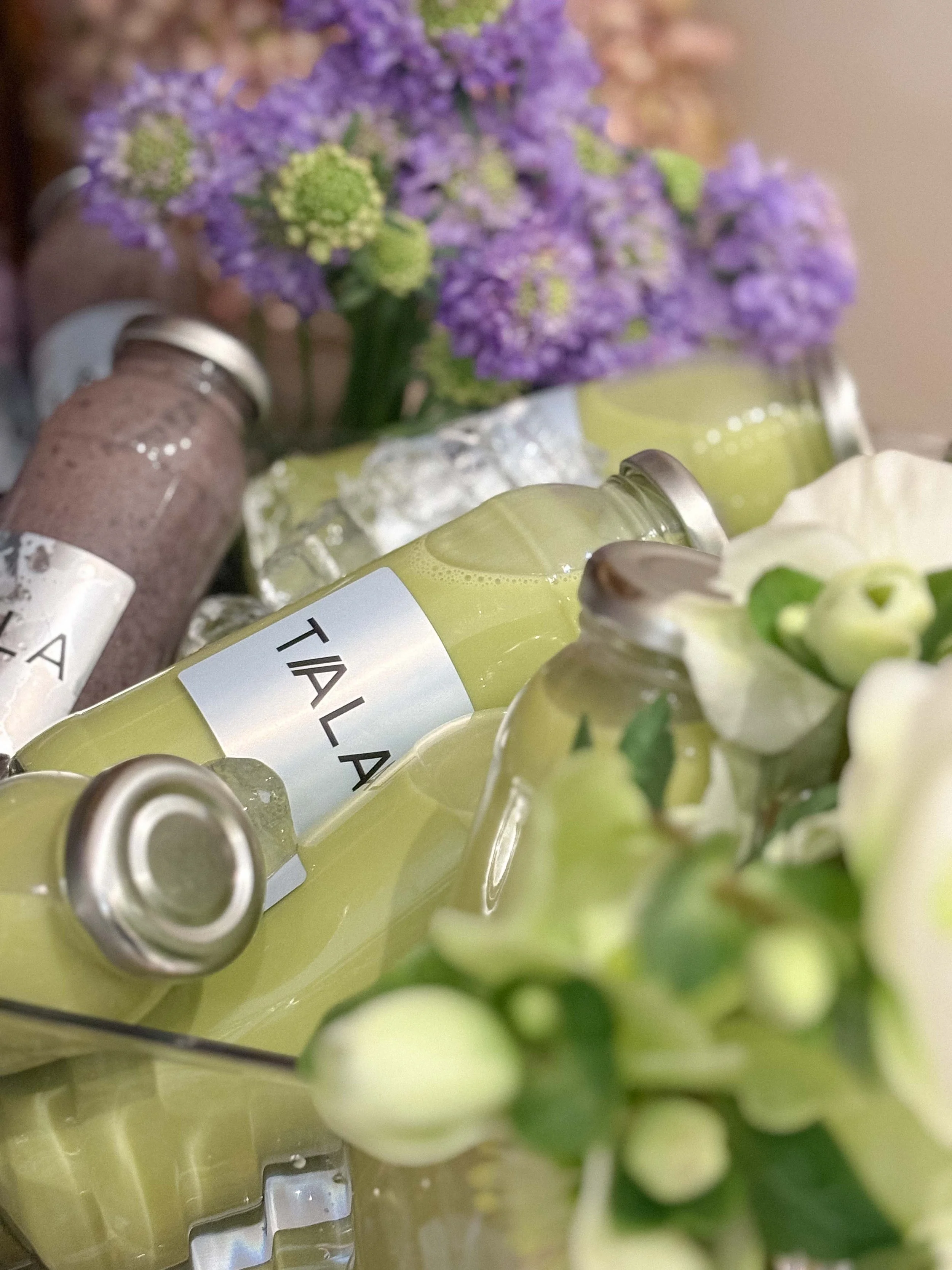 Bottles of light green and purple milkshakes or beverages surrounded by purple and white flowers.