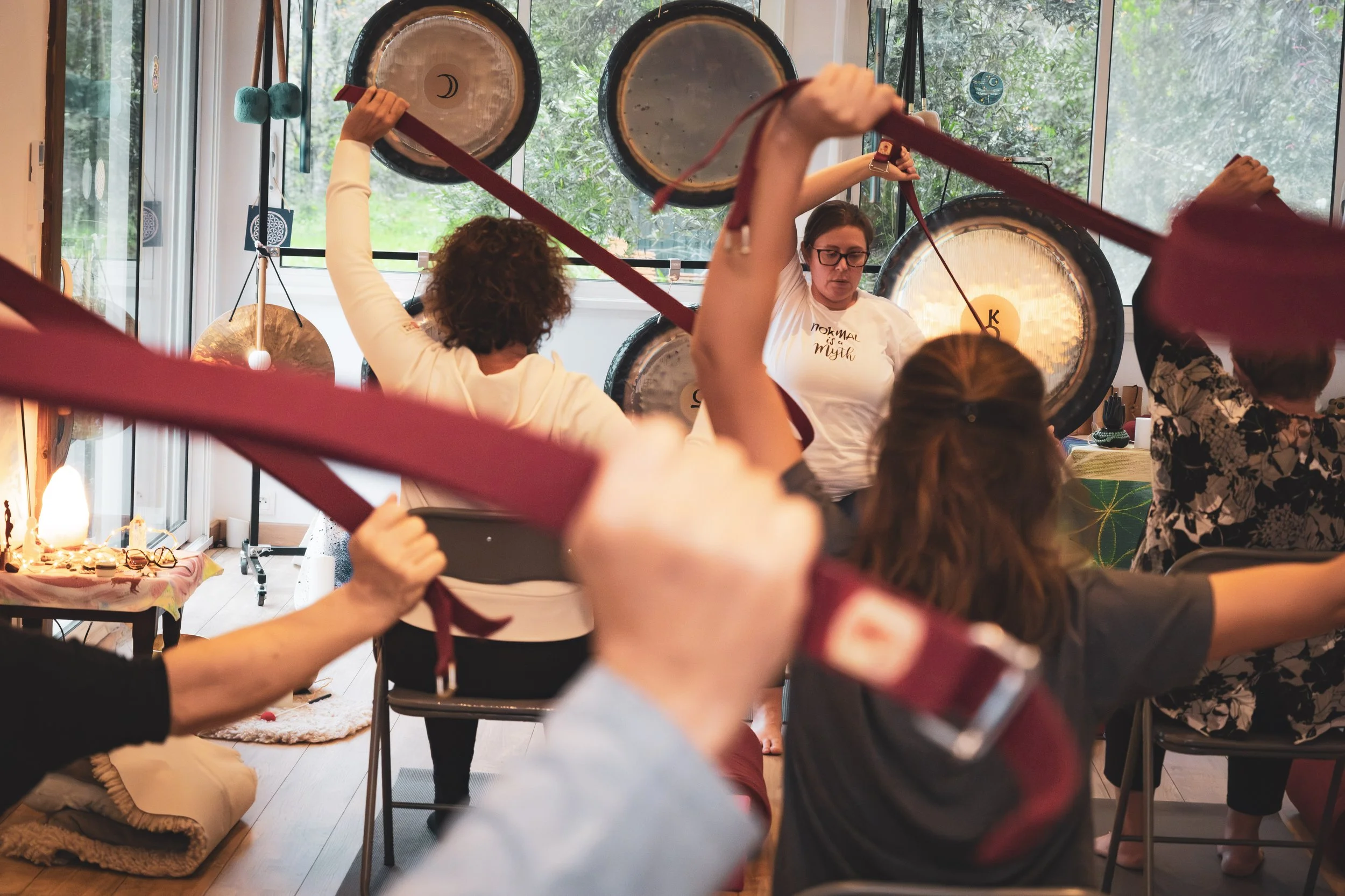 Groupe de personnes participant à un atelier de gong, avec un instructeur devant le mur de gongs, dans une pièce lumineuse avec des fenêtres donnant sur un espace vert.