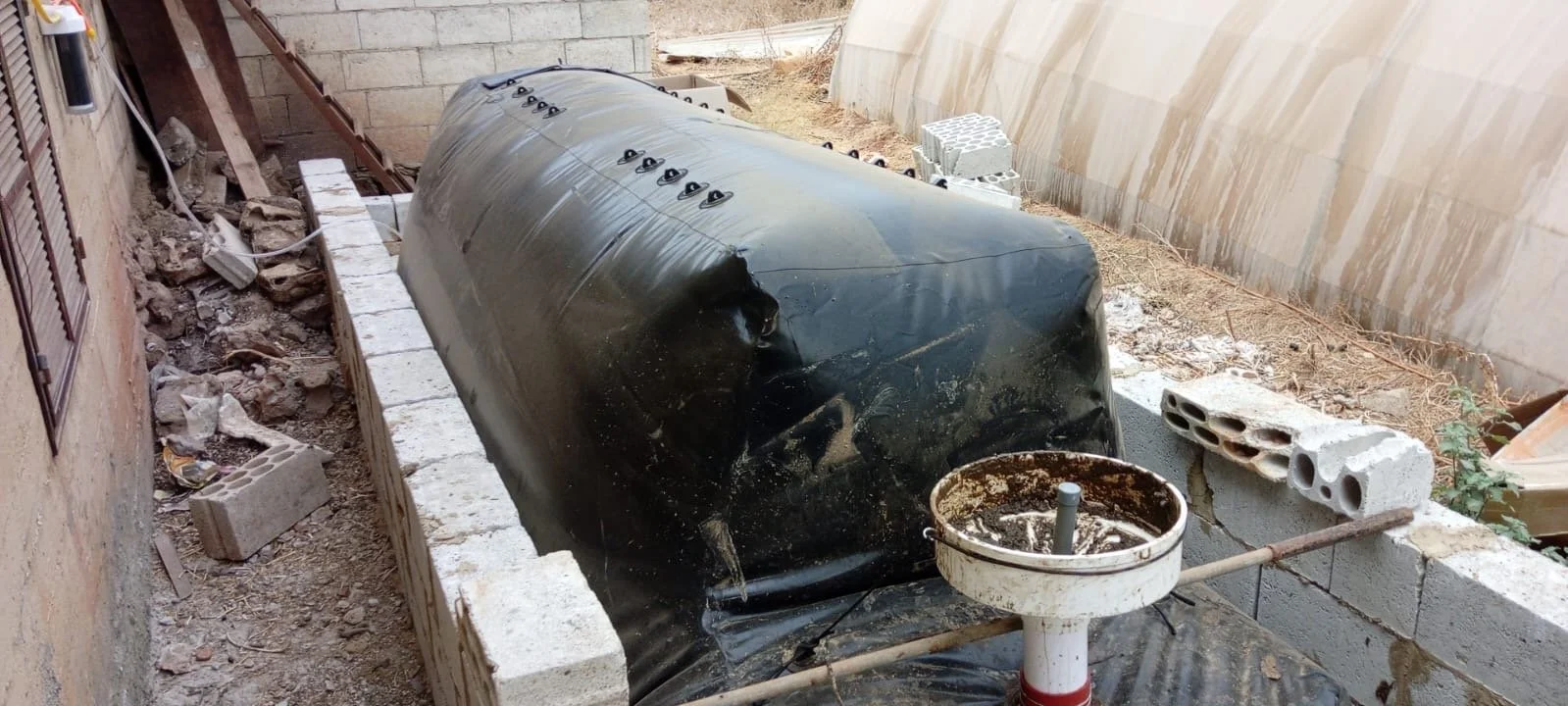 Landscape with trees, a pile of soil or mulch, and an agricultural machine partially covered with a tarp at sunset.