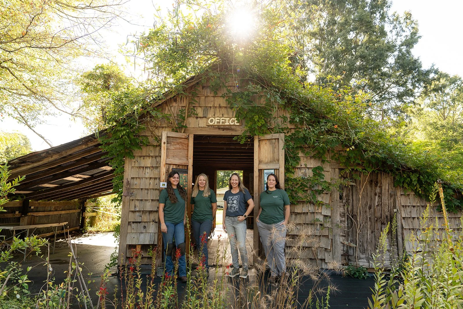 Four Southern Branch Nursery team members standing in front of a rustic wooden building labeled 'Office', with sunlight shining through trees.