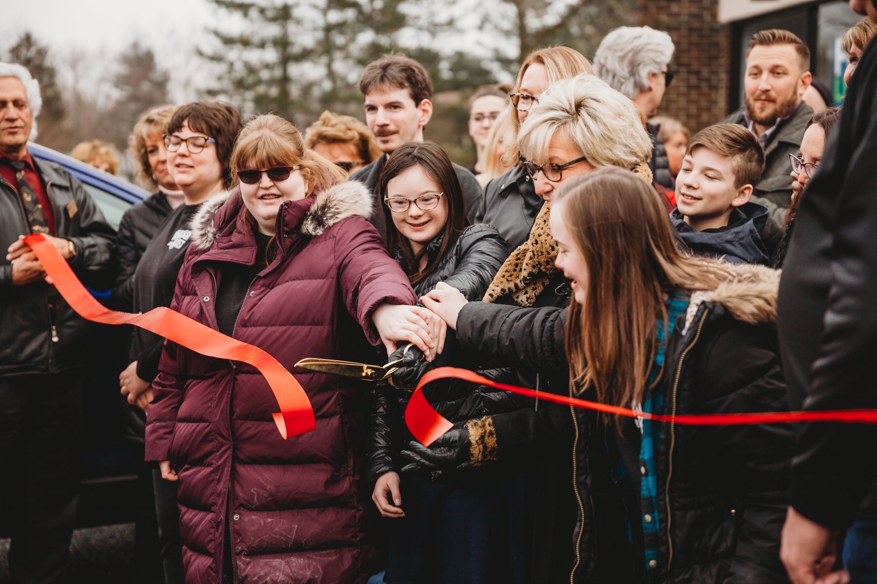 A large crowd of people outside cutting a large red ribbon.