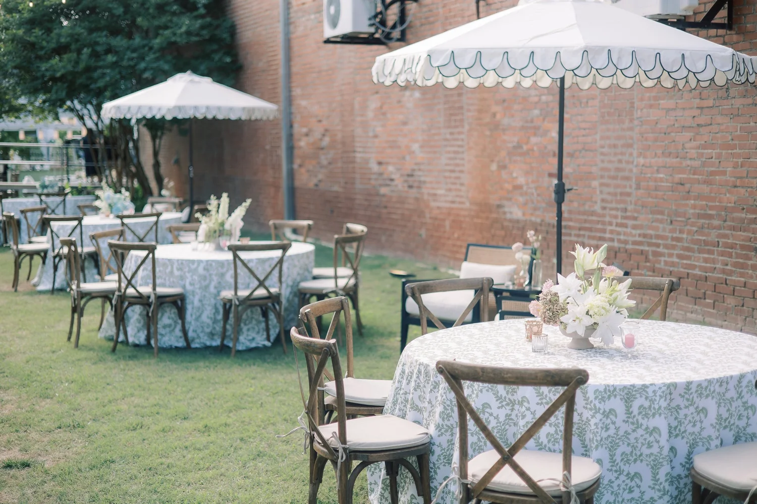 Coordinated wooden crossback chairs and dressed reception tables beneath custom scalloped parasols