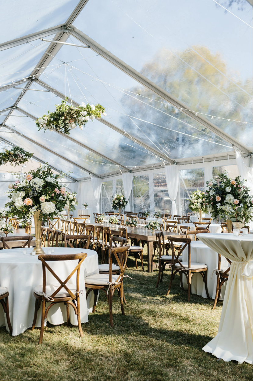 Reception under clear tent with wooden cross-back chairs