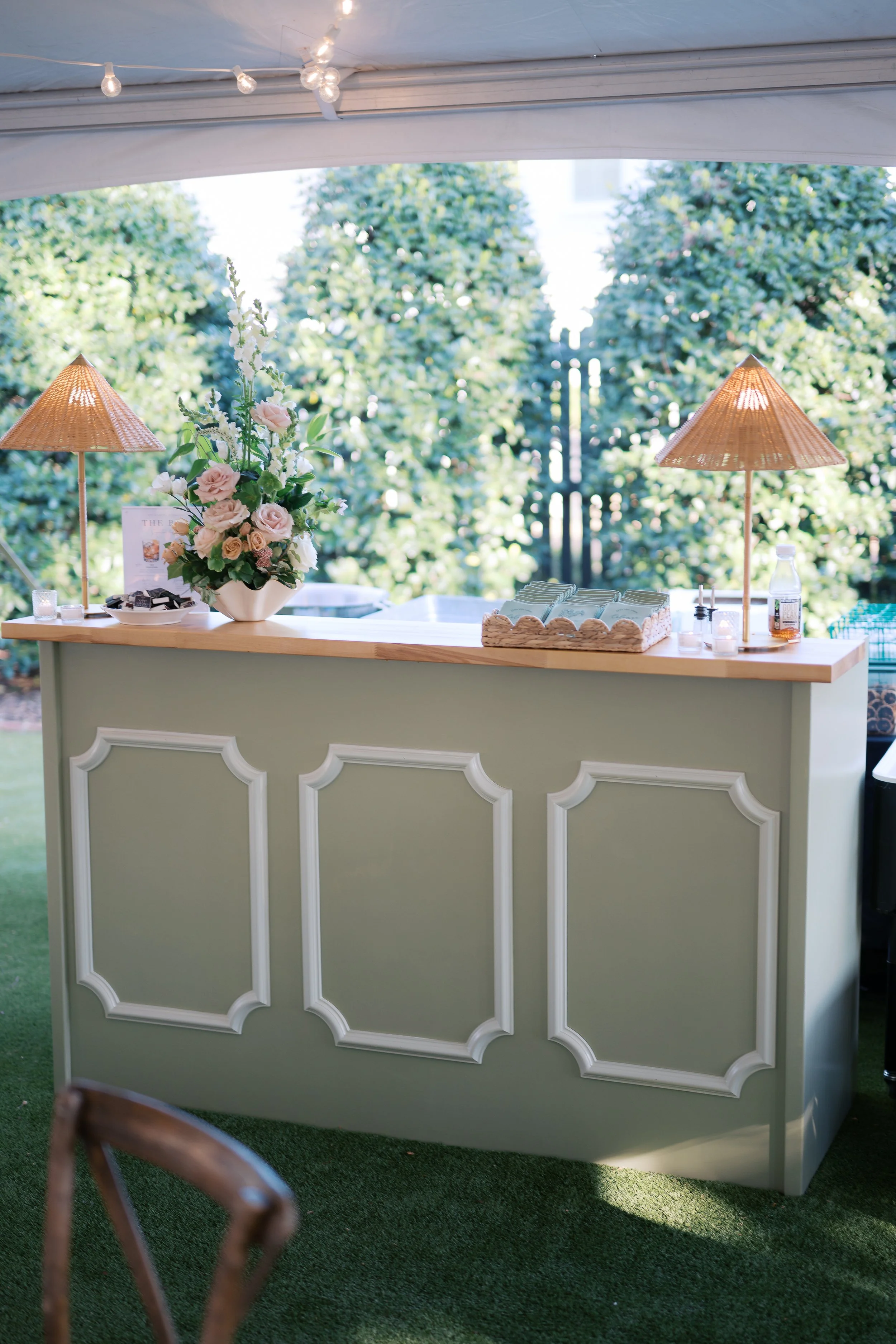 Sage-green paneled custom bar with coordinating lighting and floral design