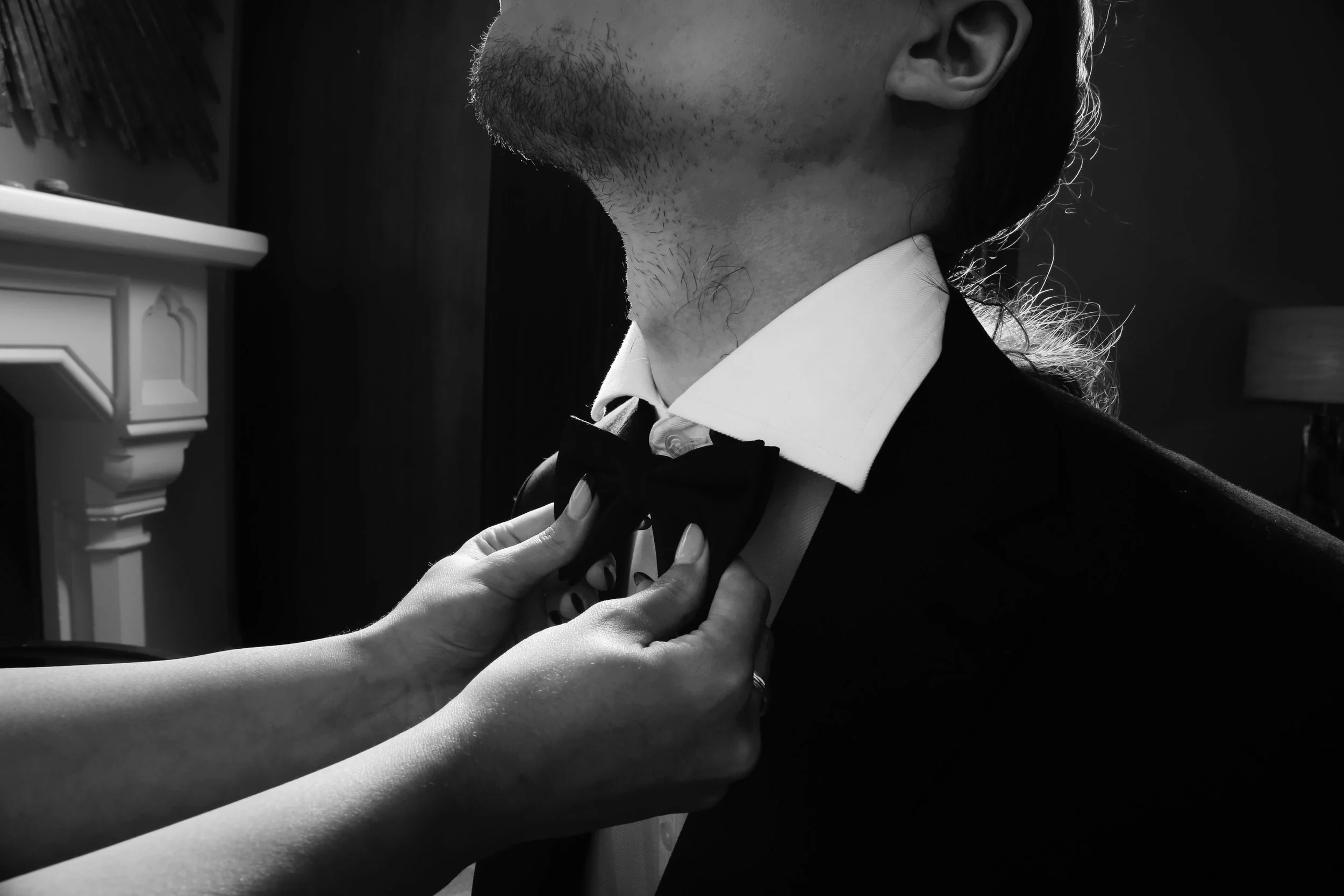 Person adjusting bow tie on a man wearing a tuxedo, white shirt, and bow tie.