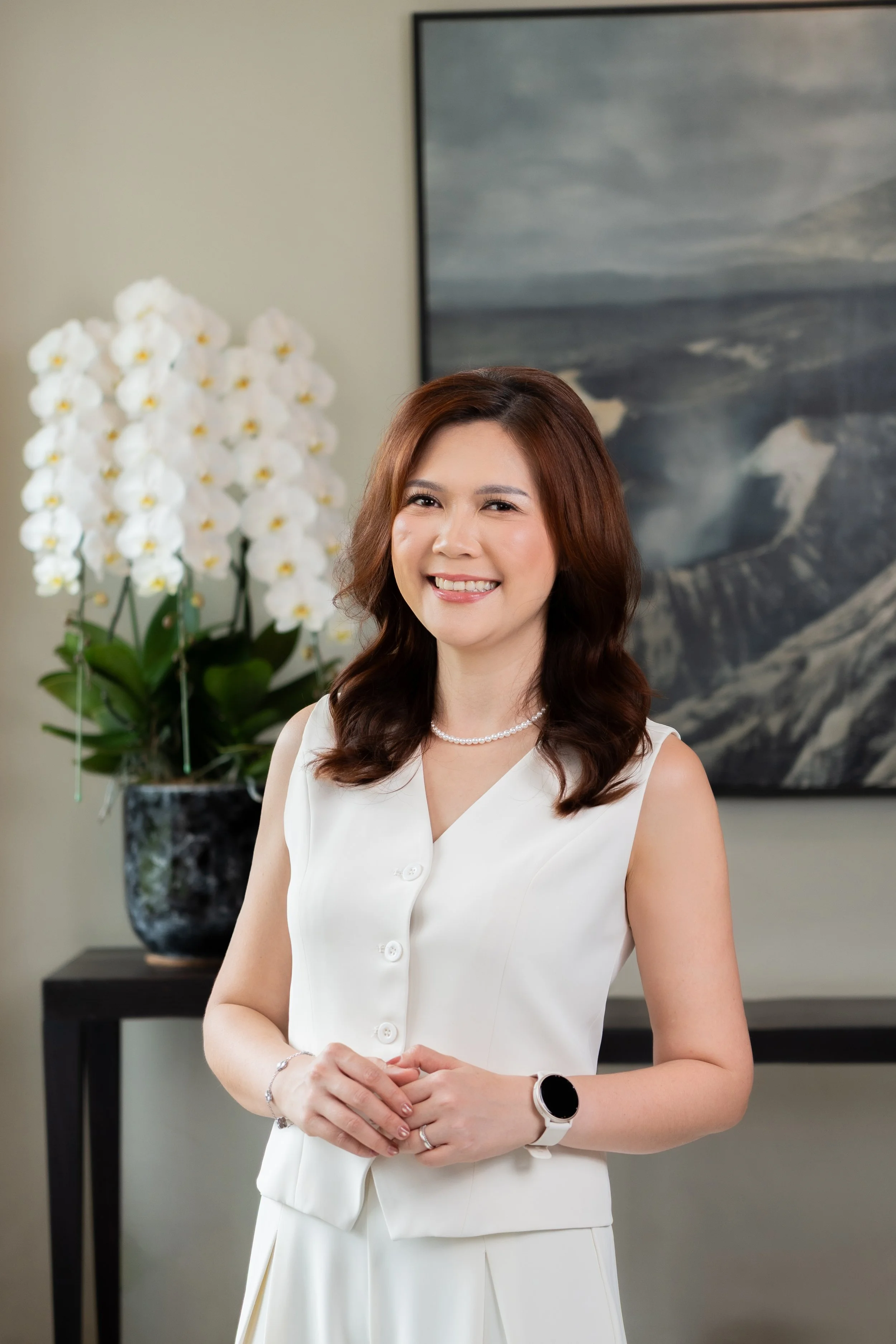 Liwi Wardhana & Co smiling in front of a large colorful painting of a landscape with green fields and blue sky.