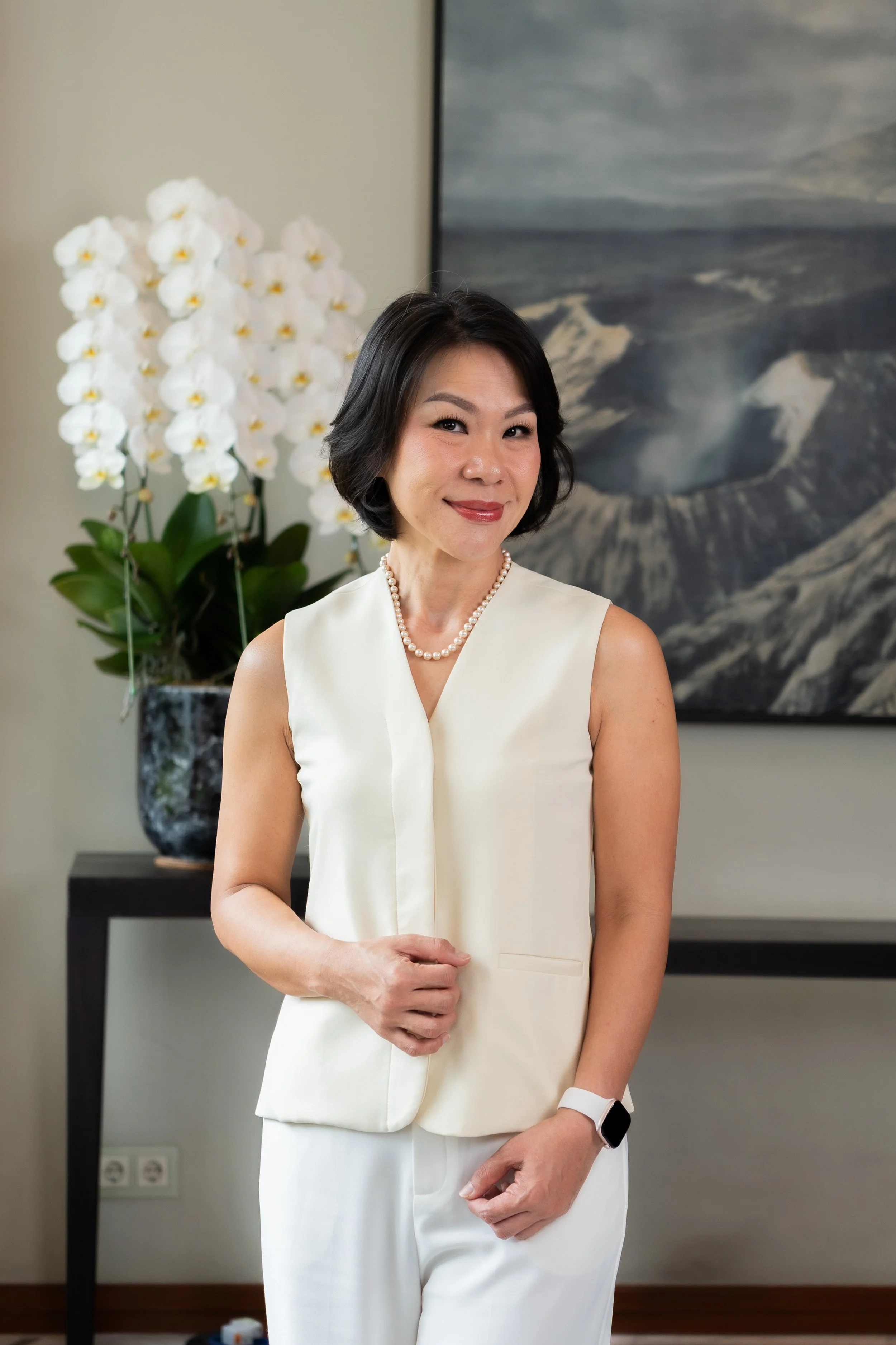 Keny Wardhana & Co with short dark hair, wearing a shiny beige blouse, standing in front of a large, colorful abstract artwork.