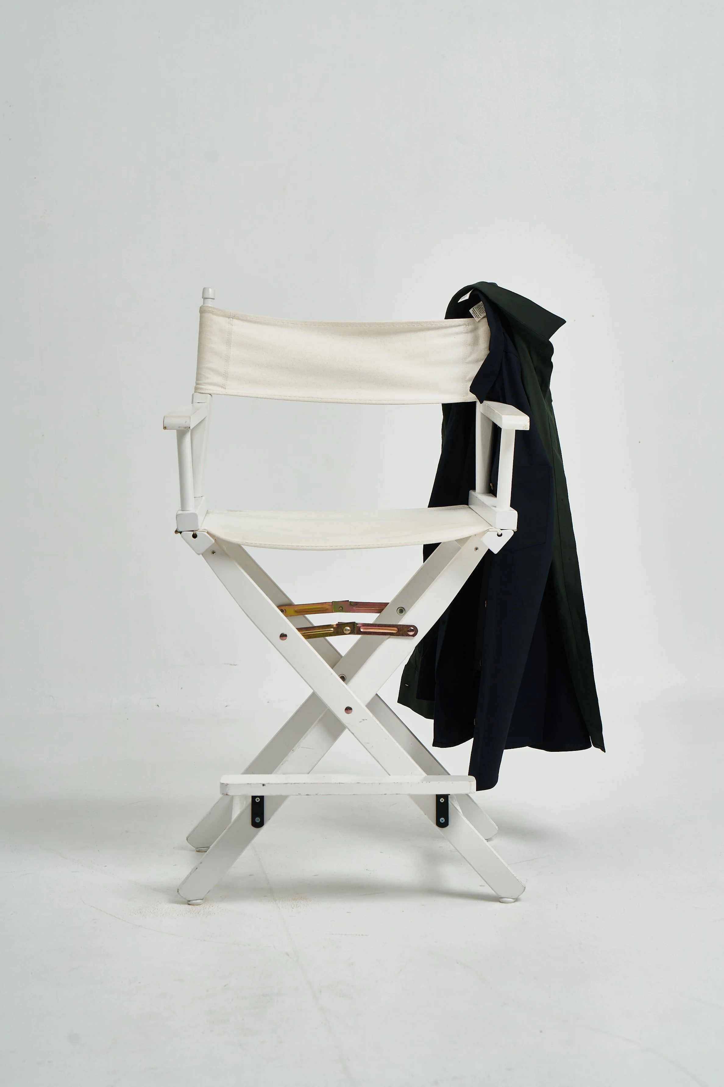 A white director's chair with black and green clothing draped over it, set against a plain white background.