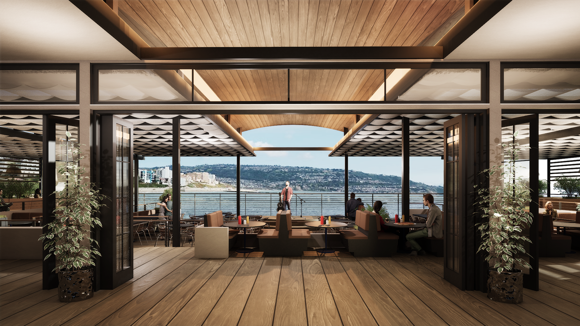 View of a restaurant with large windows overlooking a body of water and distant shoreline, inside and outside seating areas, and people dining and walking outside.
