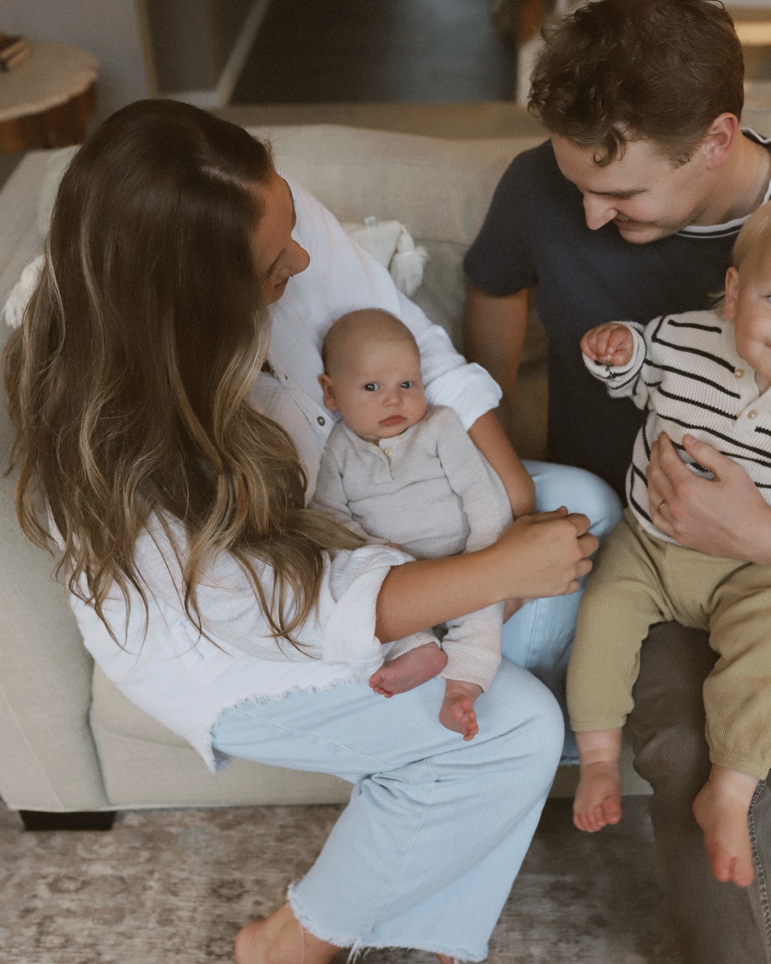 A woman sitting on a couch holding a baby, with a man and another child nearby, in a cozy living room.