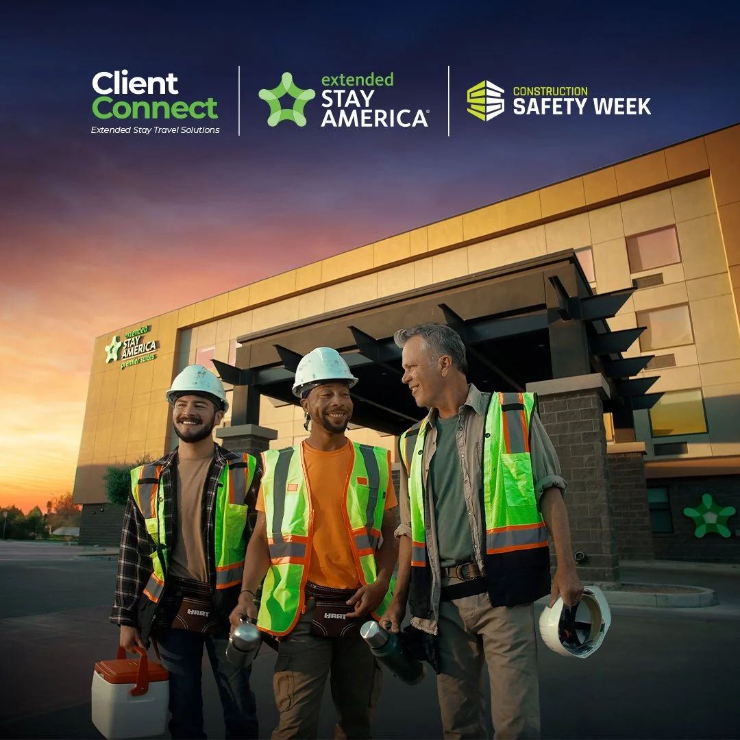 Three construction workers in safety vests and helmets standing in front of a building with a sunset sky in the background, smiling and talking.