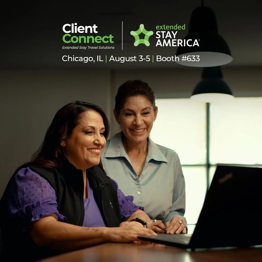 Two women smiling and looking at a laptop screen during a business meeting or event.