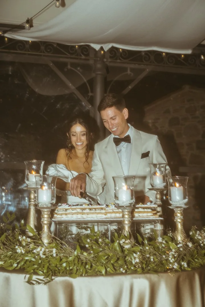 A bride and groom cutting their wedding cake at reception with candles and greenery decorations.
