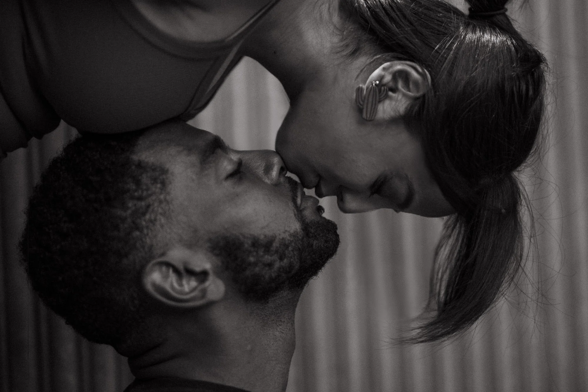 A close-up black and white image of a couple engaging in an intimate moment, about to kiss, with their faces very close together.