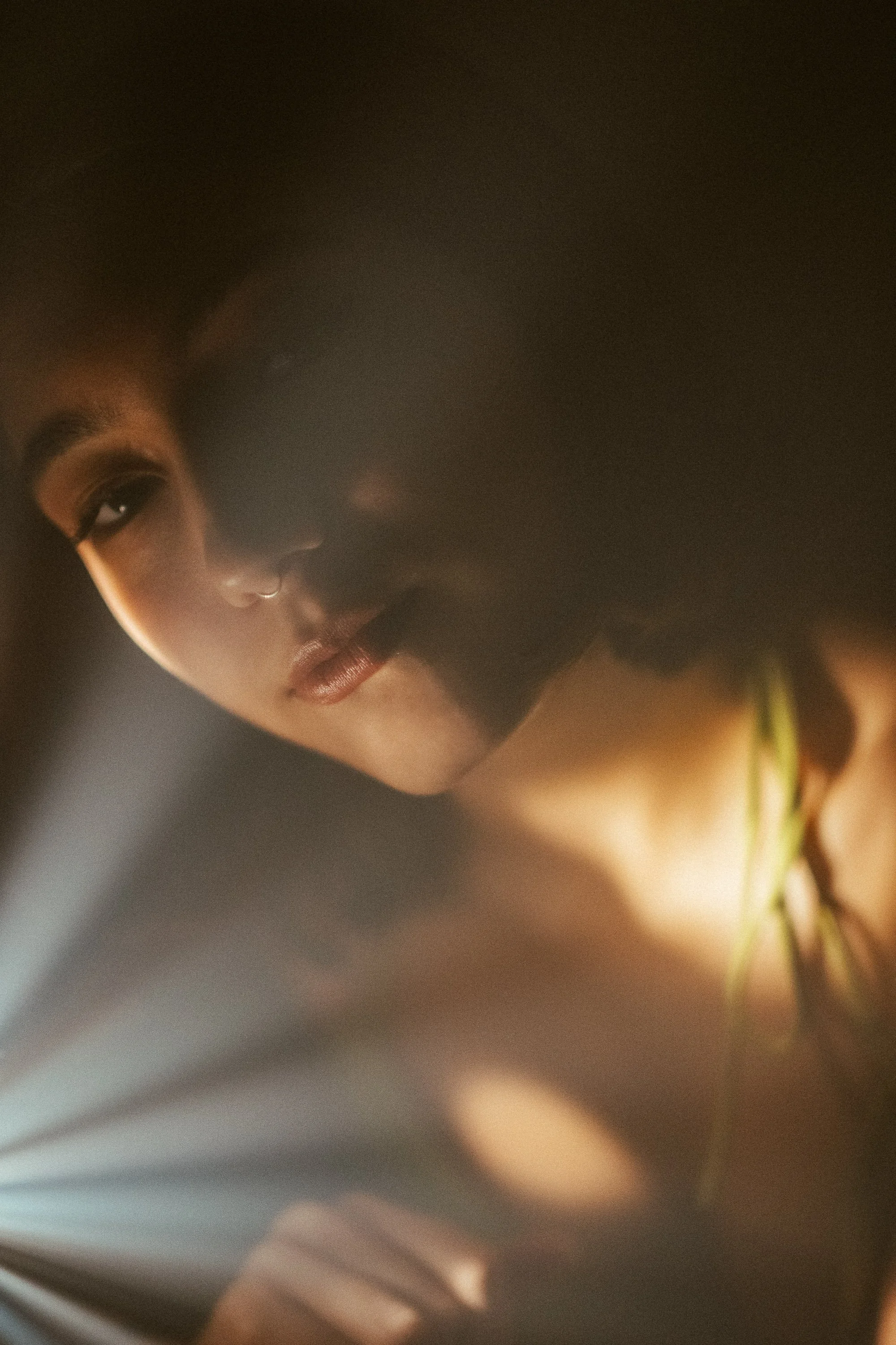 A close-up of a woman with dark hair, tan skin, and a septum piercing, looking down over a partially open book in a dimly lit setting.