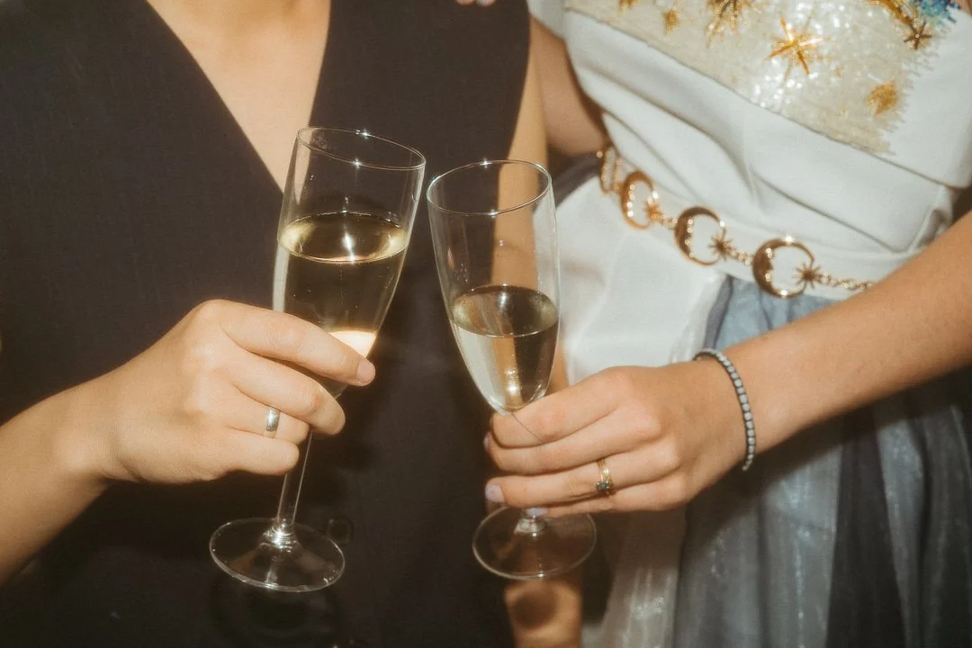 Two women in elegant attire clink champagne glasses filled with sparkling wine at a celebration.