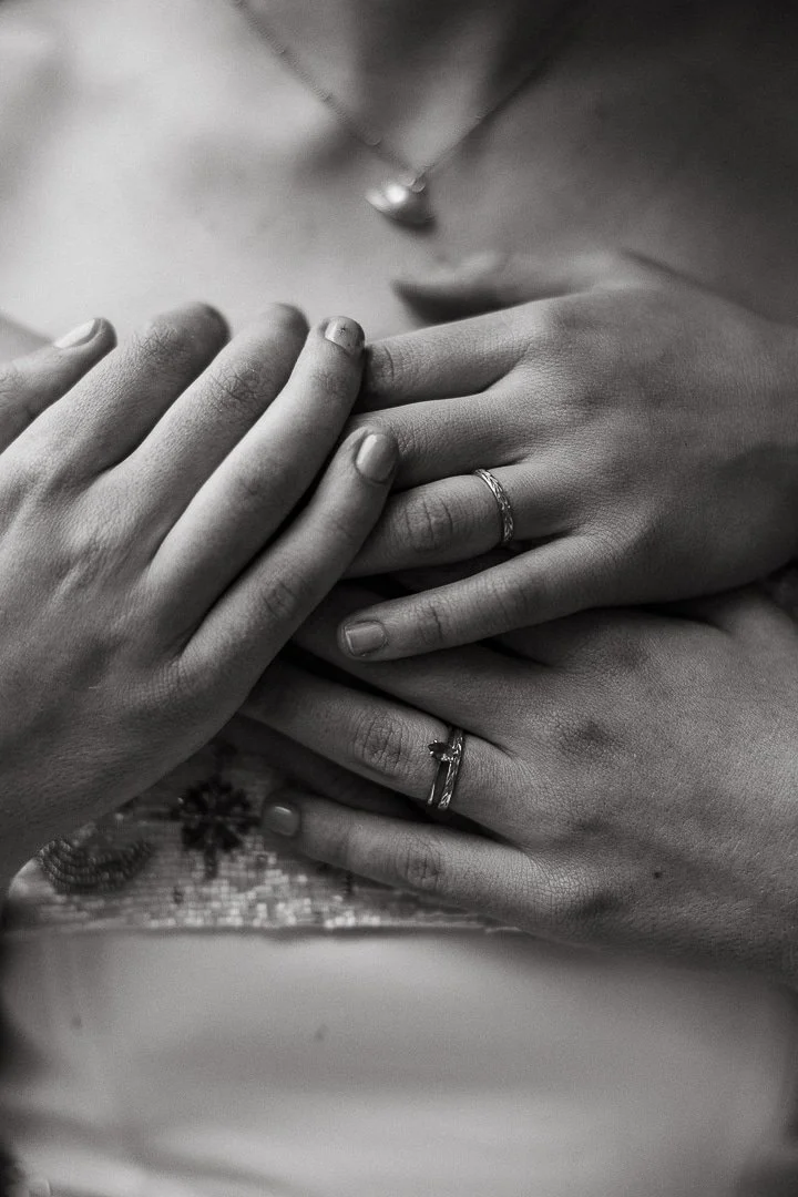 Close-up of two people’s hands with wedding rings, overlapping each other on a fabric surface, black and white photo, intimacy and connection.