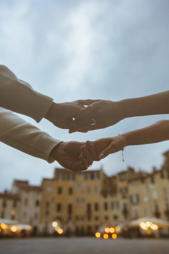 Two people holding hands with a cloudy sky and city buildings in the background.
