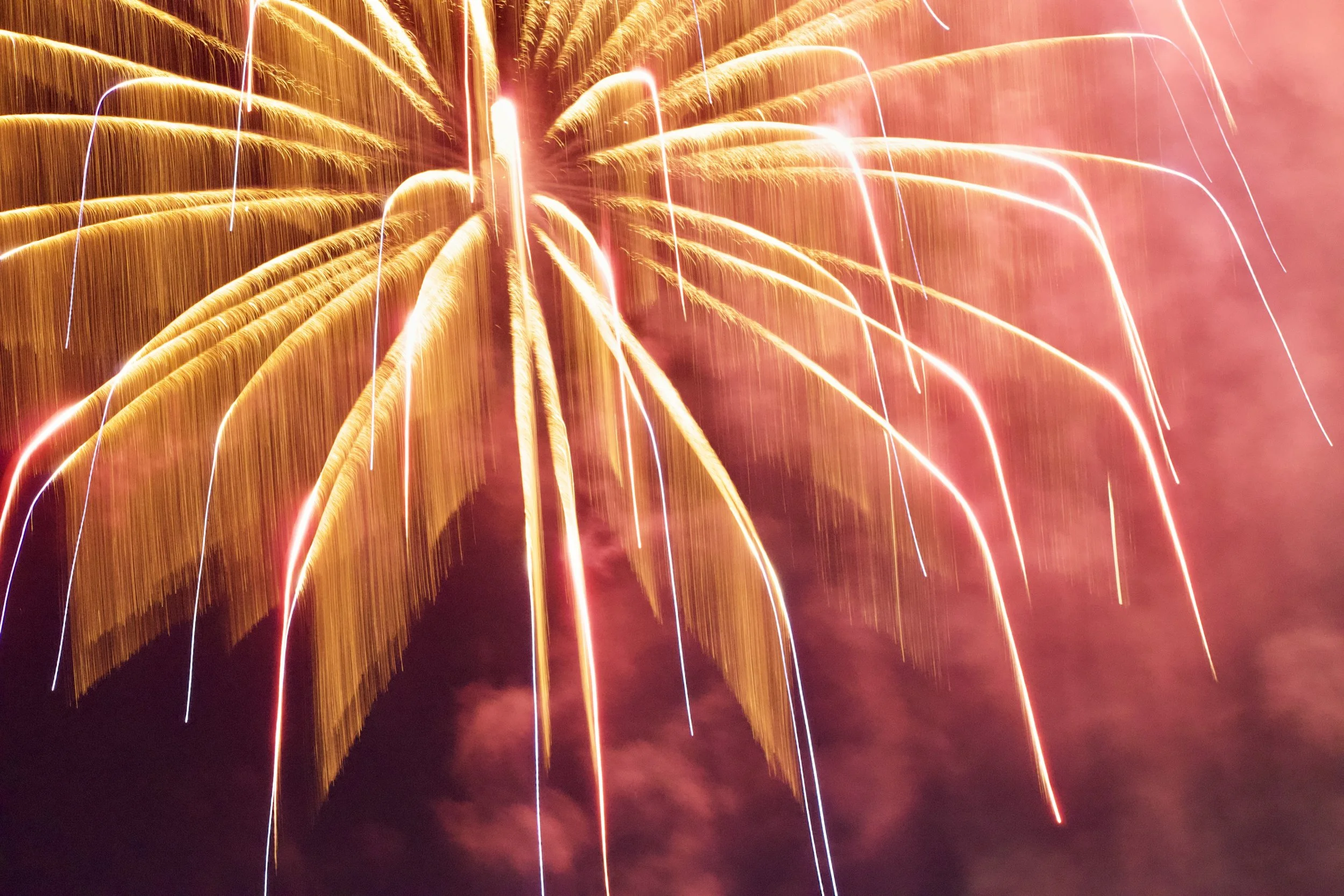 Bright orange and yellow fireworks explode in the night sky, creating streaks of light against a dark background.