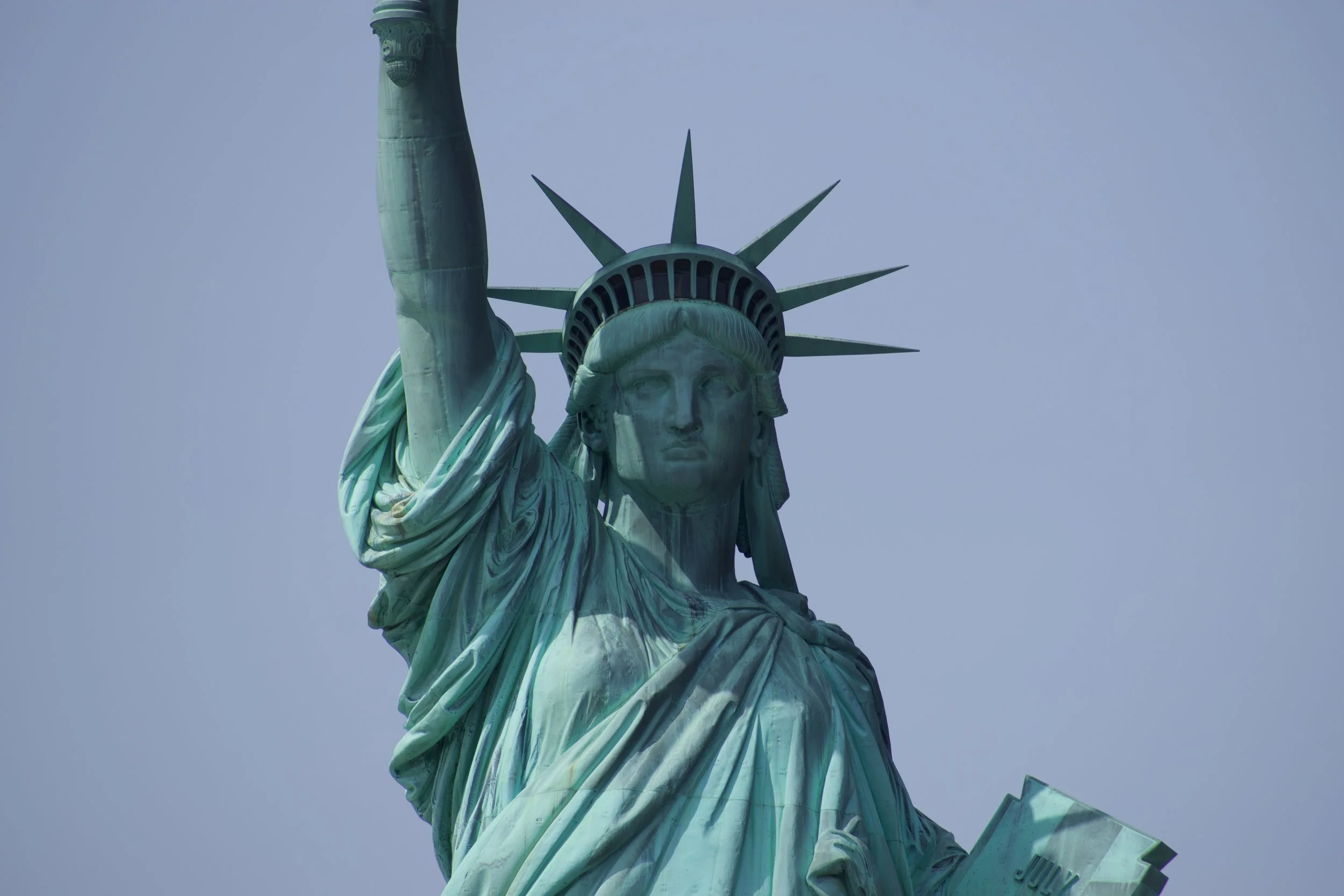 Close-up of the Statue of Liberty's face, crown, and torch, set against a clear blue sky.
