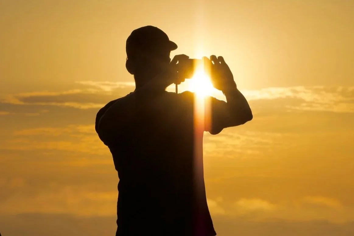Silhouette of a person taking a photo at sunset with the sun in the background