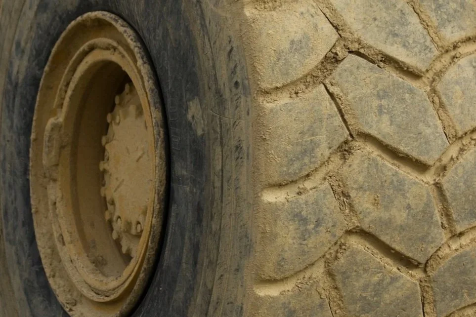 Close-up of a large tire with a muddy, patterned tread on a vehicle or construction equipment.